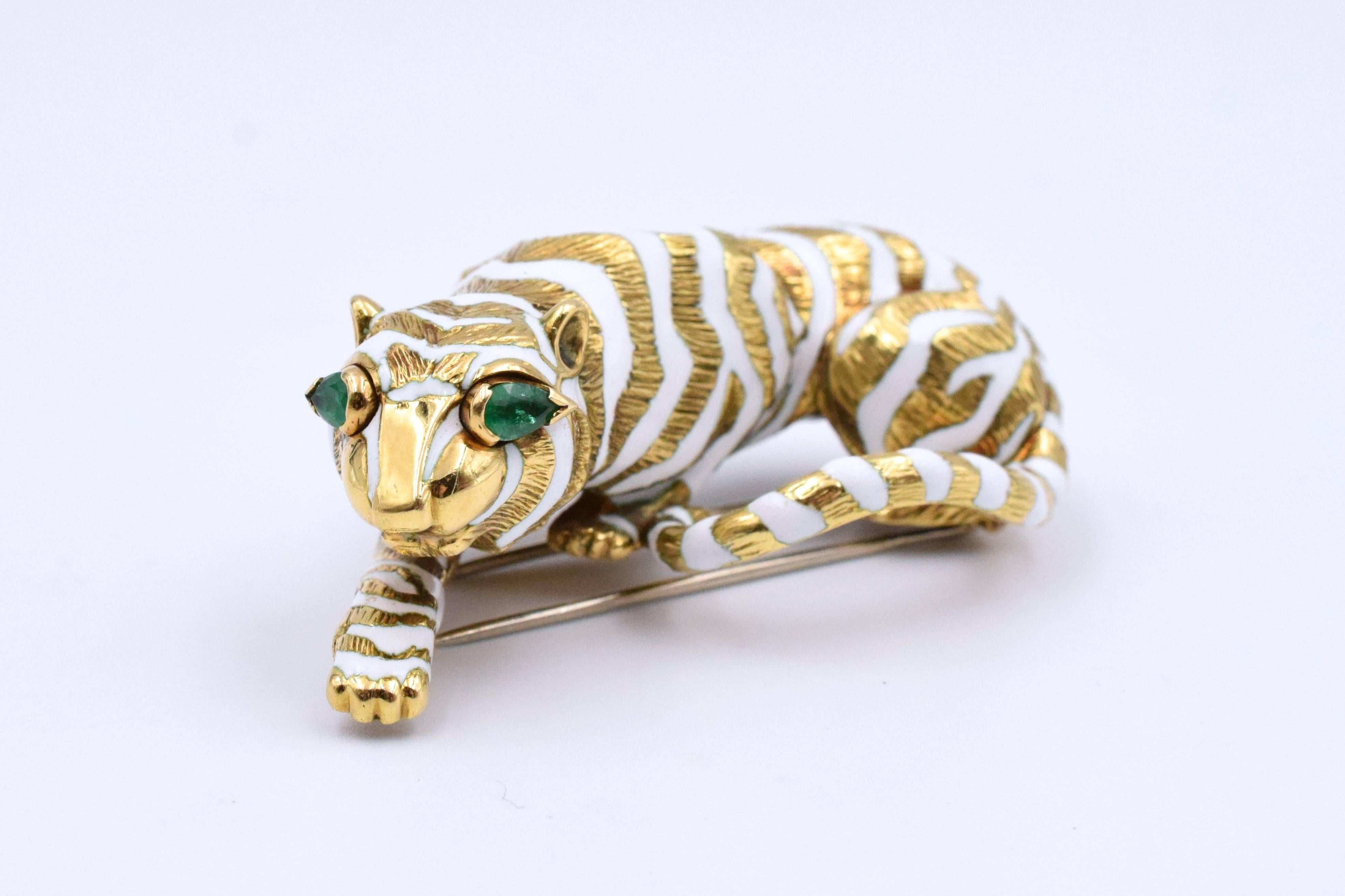 Bold look of David Webb iconic tiger brooch with white enamel & gold stripes.
Vibrant green emerald eyes  in 18k gold.
Signed & marked. David Webb
Measurements: 55mm x 30mm