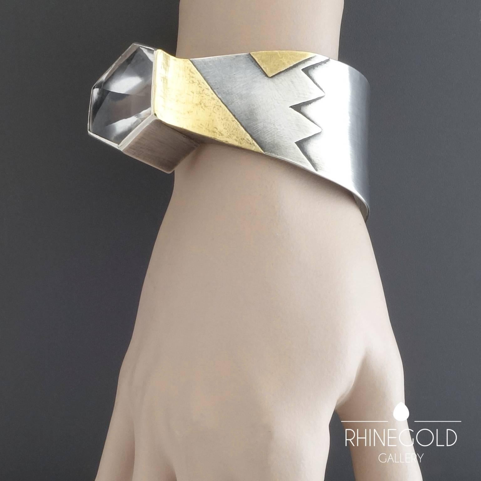 Rainer & Sabine Loewe, Germany: 1970s Modernist Rock Crystal Gold Silver Cuff Bangle
Sterling silver, 22k yellow gold, rock crystal; weight approx. 95.6 grams
Outer size 7.9 to 6.1 cm (approx. 3 1/8” to 2 3/8”); width max. 3.8 cm (approx. 1 ½”);