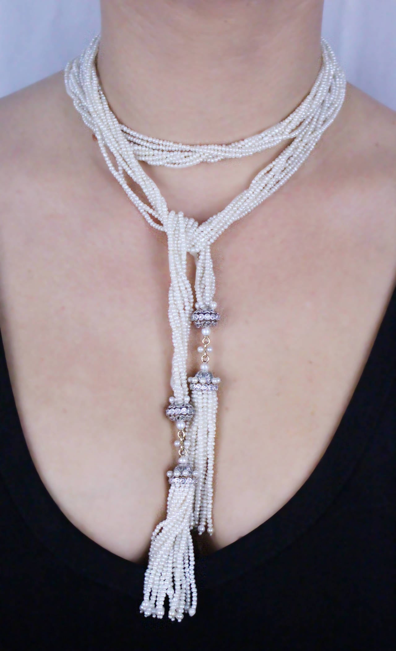 Necklace composed of seven strands of seed pearls with open work diamond-set beads leading to 2 tassels with a total of 32 strands of seed pearls with diamond caps. 80 old miner cut diamonds weighing approximately 1.25 carats.

The total length of