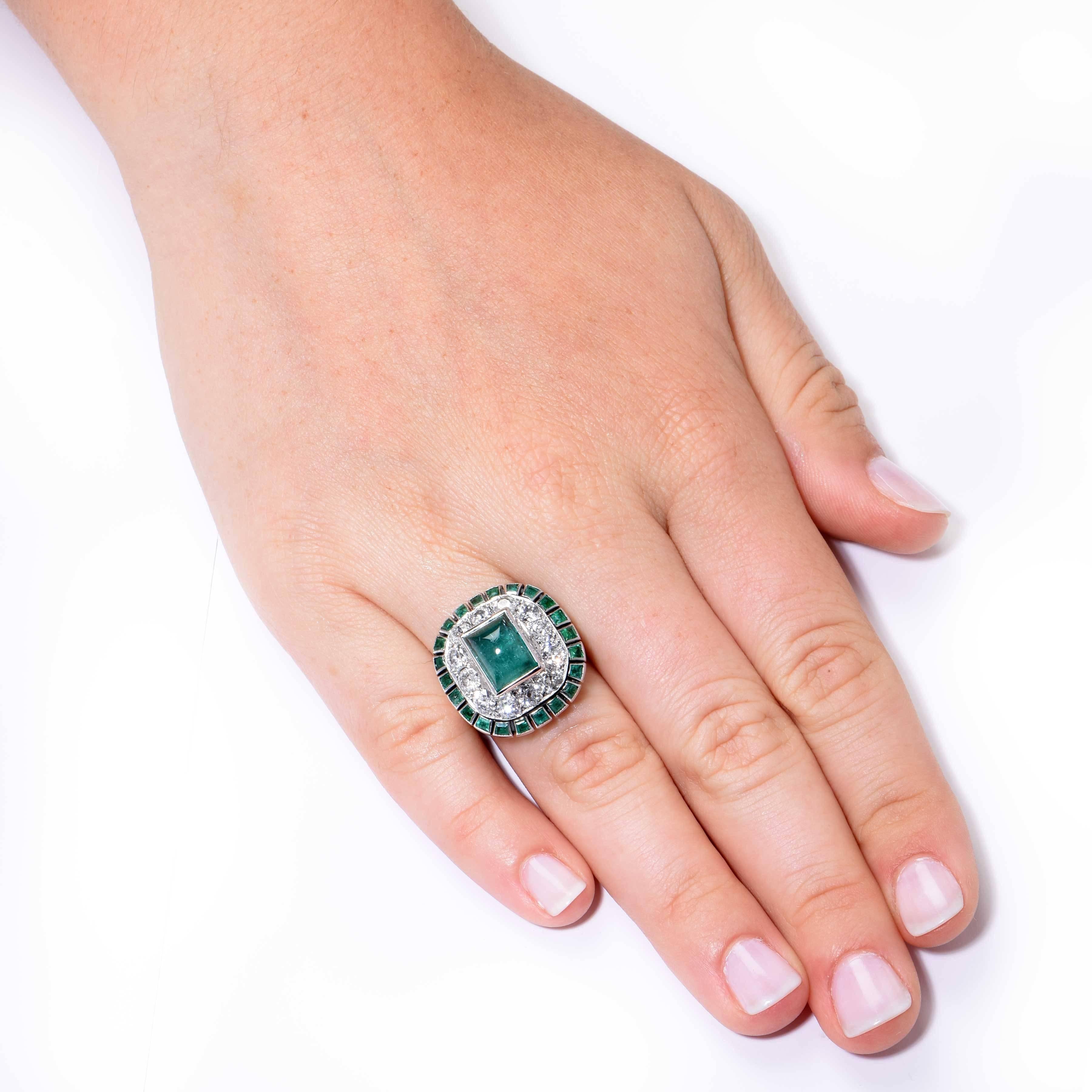 This sugarloaf cabochon bezel set emerald sits in the center, surrounded by one row of 12 Old European cut diamonds weighing approximately 1.70 carats. It is further surrounded by a row of small bezel set emeralds. 

Size 8 1/2  (Can be sized)
Metal