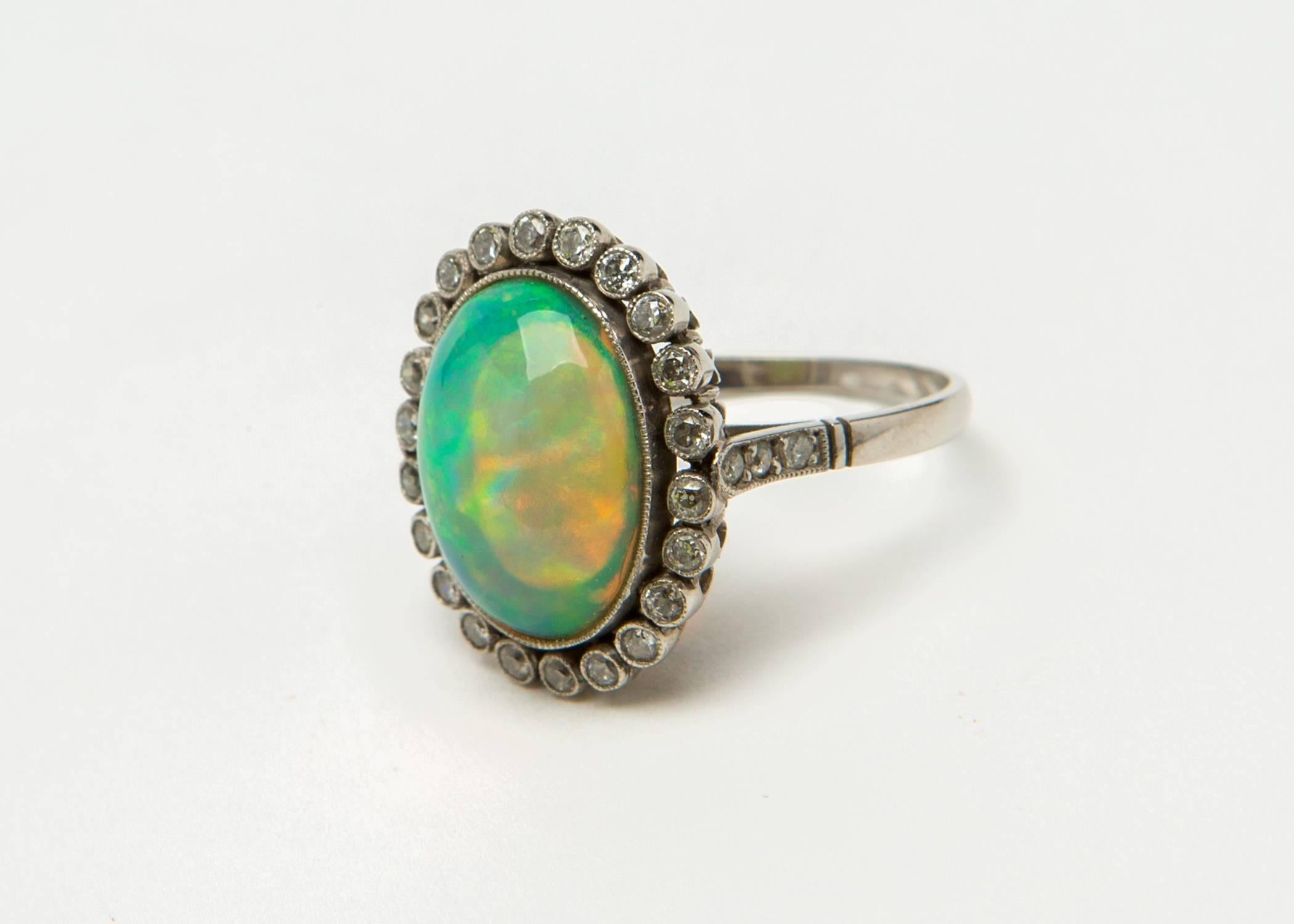 This extremely bright opal has significant flashes of green and blue and secondary orange coloration. The platinum mounting with vintage design detailing is set with a full circle of diamonds. The top of the ring is 3/4's of an inch in length. The