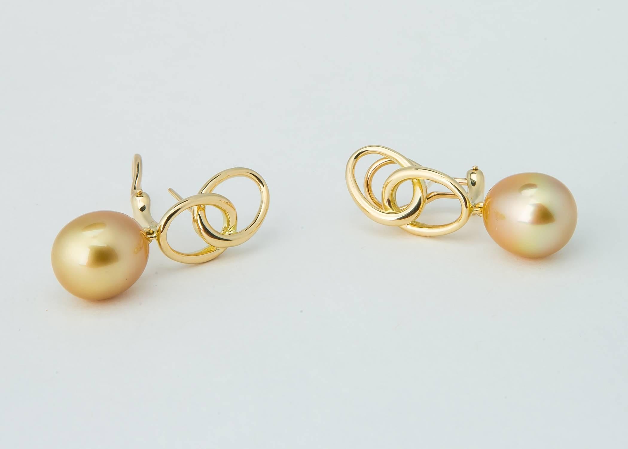 Elsa Peretti has always proven less is more. Rich golden south sea pearls are suspended below elegant geometric loops. Simply Chic.  The pearls measure 13.2 x 11.8 mm and the total earring length is 1 3/8's inches. 