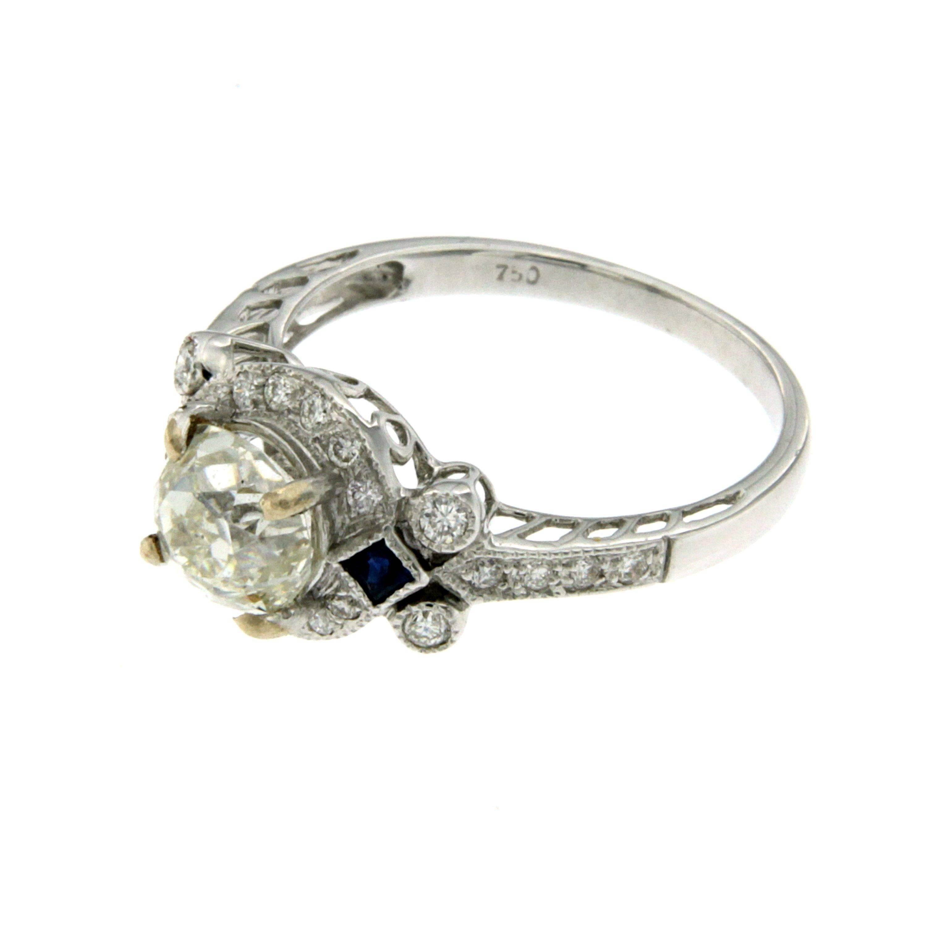 An Antique Art Deco 18k Gold Diamond & Sapphire Ring featuring a stunning 1.36ct. old mine cut Diamond graded I color VS2 clarity, it is surrounded by 24 colorless diamonds weighing 0.26ct. . There are also two 0.10 carat briolette cut Sapphires
