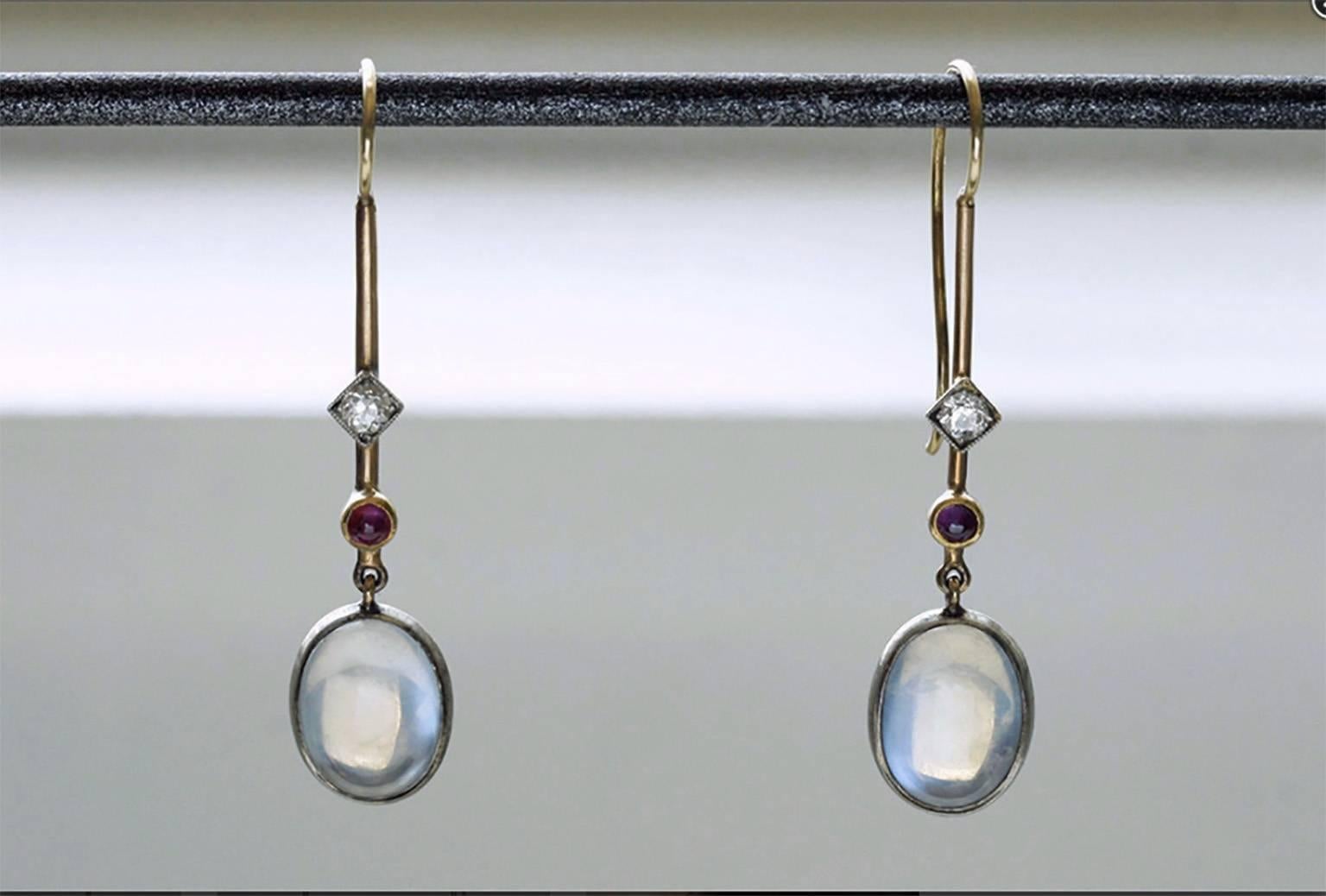Edwardian 'Skate-Blade' long drop moonstone earrings with platinum-set small European cut diamond and ruby cabochon. The earrings are 14k gold, and the foil-backed moonstones reflect the light beautifully.  

Total Drop: Approximately 1.75”