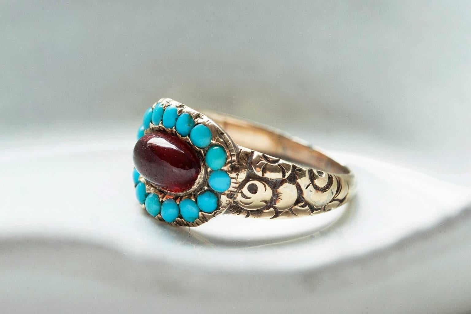 A Georgian turquoise and cabochon garnet ring. Originally the center locket of the ring had had woven hair, but a beautifully cut cabochon garnet has replaced it. The gold shank has decorative chased flowers, and the ring is 14k yellow gold. 

US