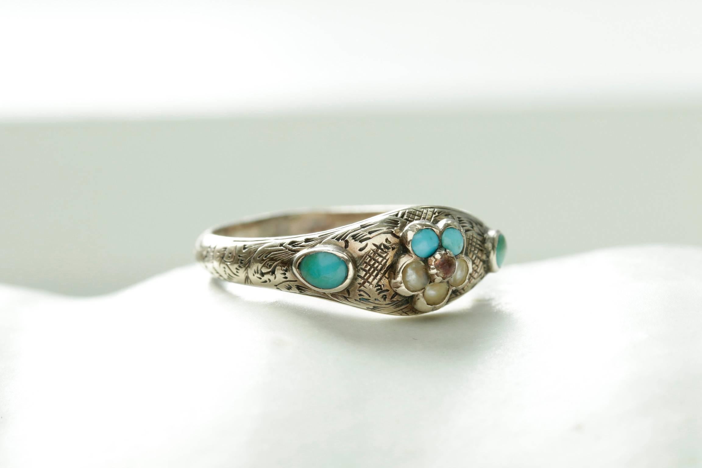 A very pretty late Georgian Forget Me Not ring with beautiful engravings. The flower is set with two turquoise stones, three split pearls and a ruby paste in the center, and the extra turquoise stones on each side adorn the ring. The ring is in 9k