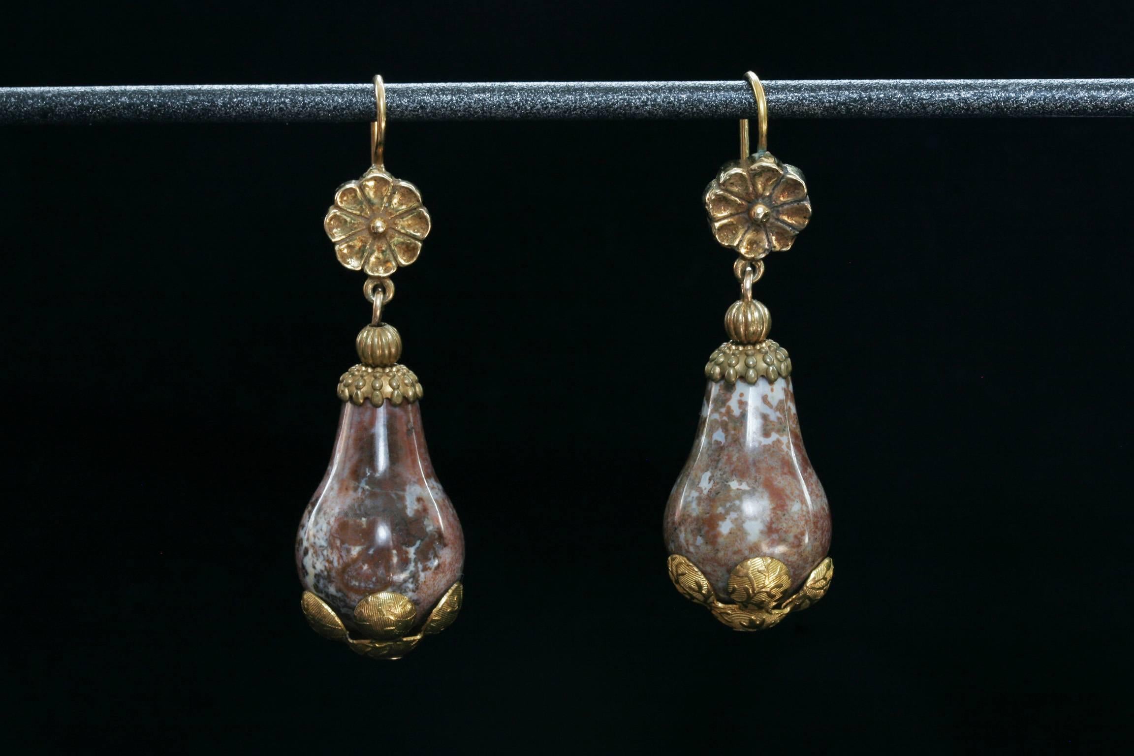 A pair of early Victorian carved agate and pinchbeck earrings. Hand-hammered flower petals wrap the bottom of the agate drop, and the top is accentuated with petite flowers. The earrings are in good condition.

Total Drop: Approximately 1.75”