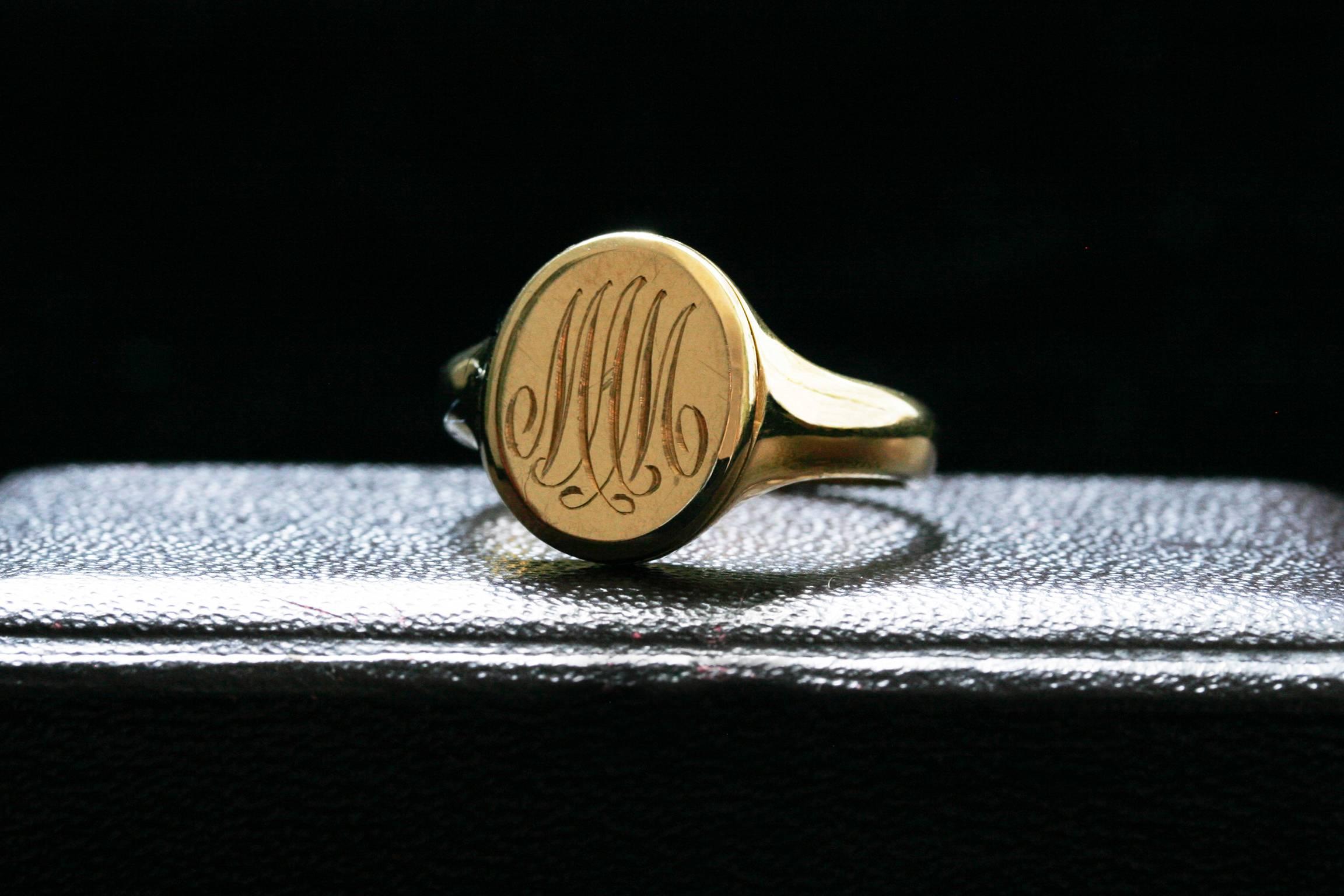 A late Victorian secret locket ring. This 18k gold signet ring was engraved with the initials ‘MAM’. London hallmarked 1897, contains a hidden hinged locket compartment to its head, which reveals a vitreous enameled photo momento. English in