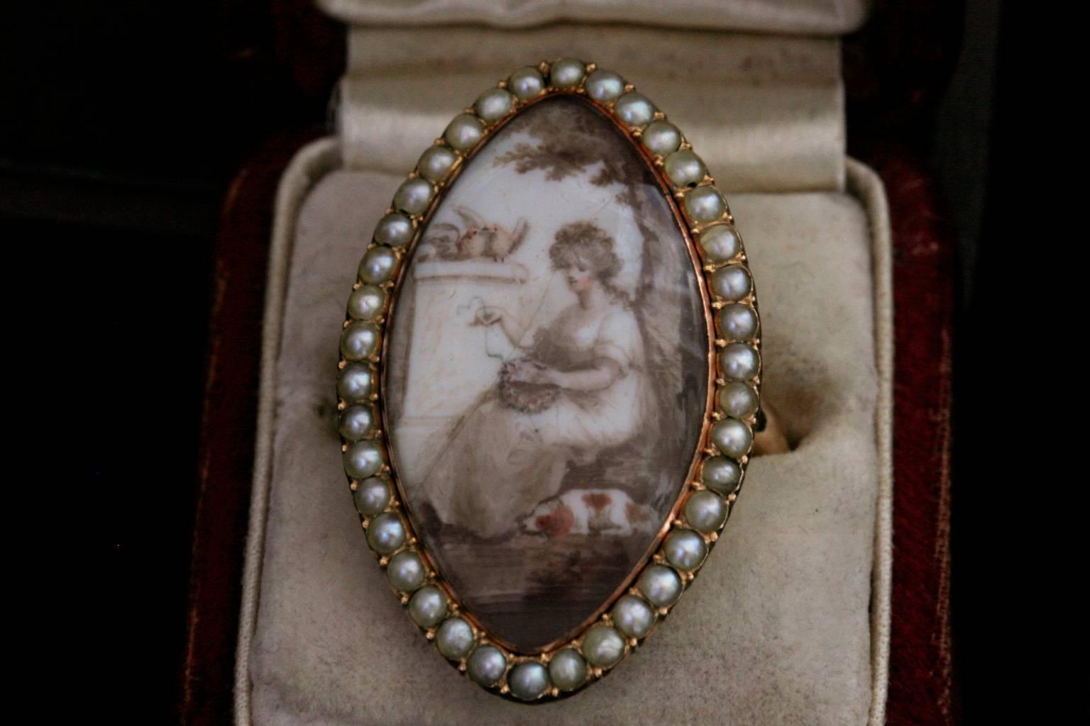 C.1800.  English in origin. This sepia miniature is made with a row of lustrous seed pearls around the navette-shaped glazed locket compartment. The miniature painting is depicting a maiden in mourning. She sits next to a plinth, accompanied by