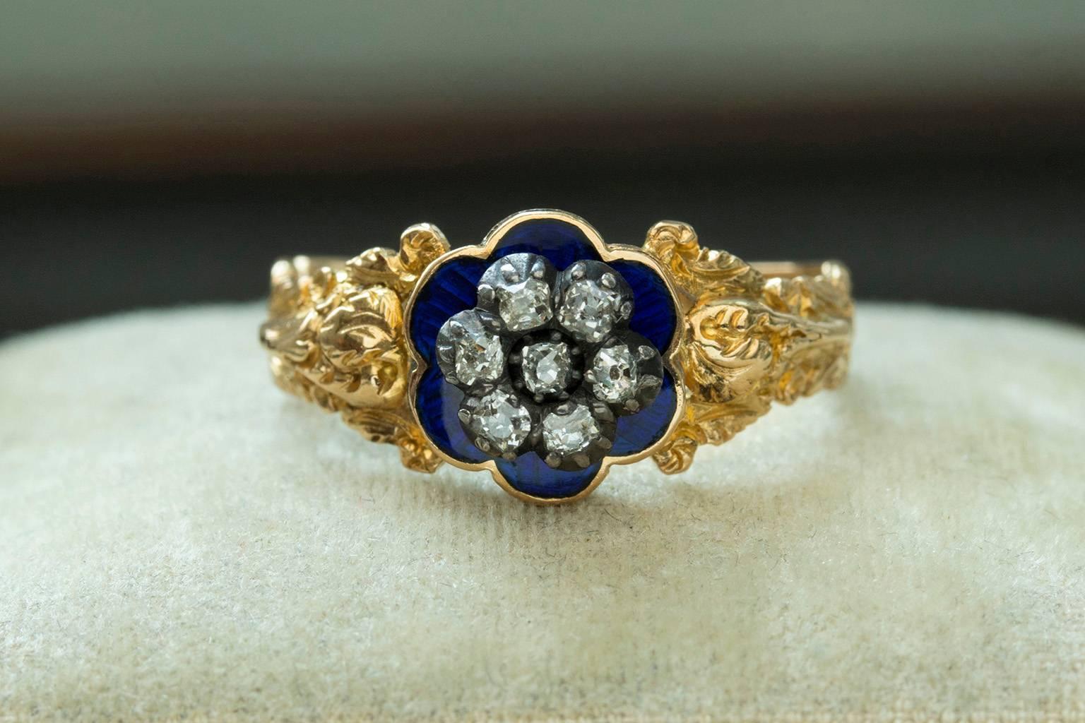 C.1828. A Georgian blue enamel and diamond ring. The center face features 'forget-me-not' flower shaped diamonds over deep royal blue enamel setting. The ring has beautifully detailed shoulders with a motif of flowers and leaves. There is an