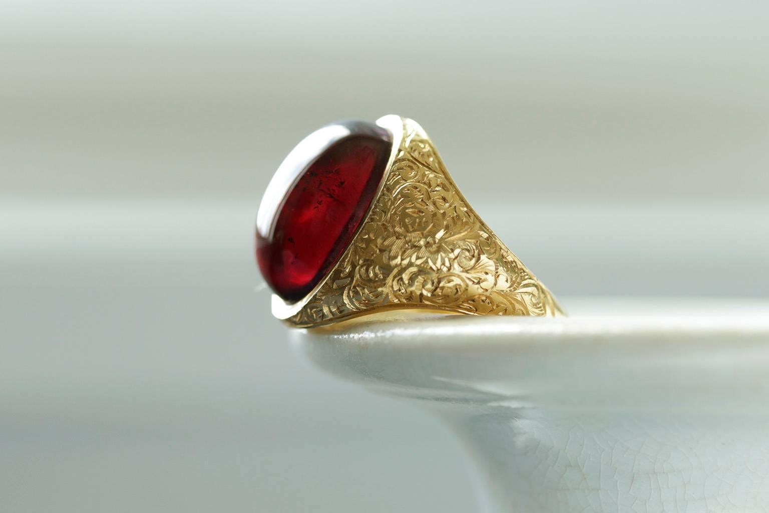 A handsome Victorian garnet cabochon gold ring. It is English hallmarked c.1852. The ring shows beautiful chasing on shoulders. With light, the garnet cabochon glows with a deep red wine hue. The sizable garnet offers a strong presence. Overall in