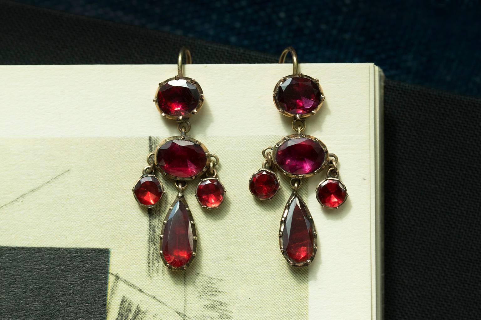 Early 19th century garnet petite girandole earrings. The stones are foil-backed, and they glow beautifully with light. The earrings test about 15k gold including the ear wires. Very easy to wear, and overall in good condition. 

Total Drop: