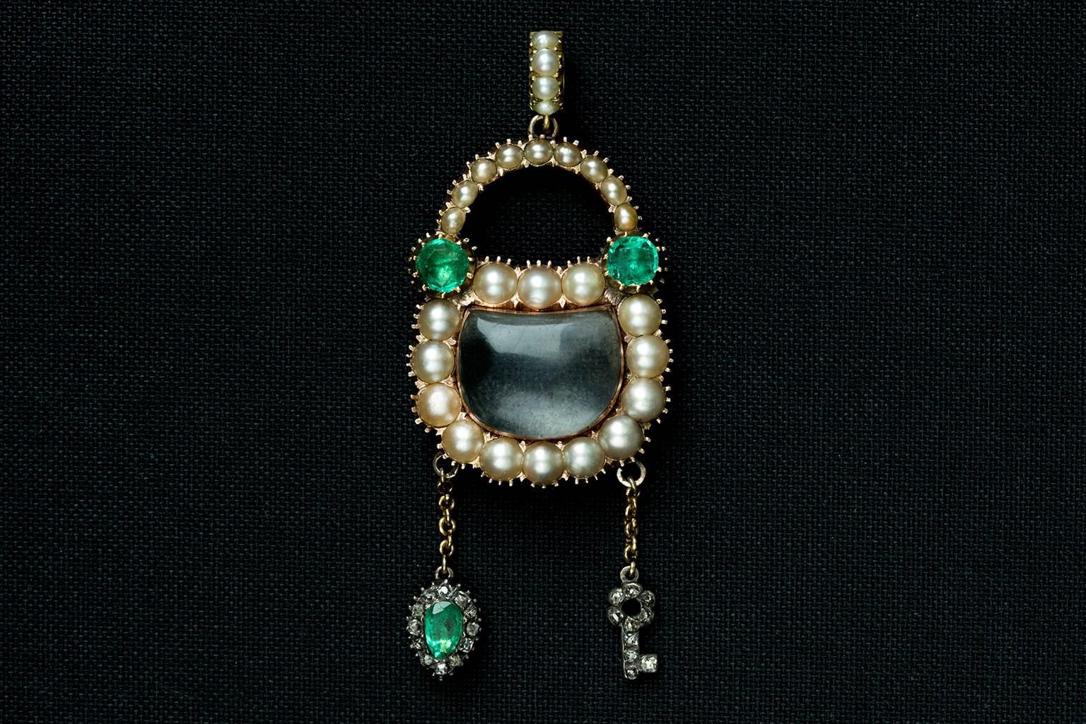 An early 19th century Georgian padlock pendant with a matching chain. The padlock is made of emeralds and pearls, and has a dangling diamond and emerald heart, and a diamond key. It also features the matching pearl bale, which makes the pendant more