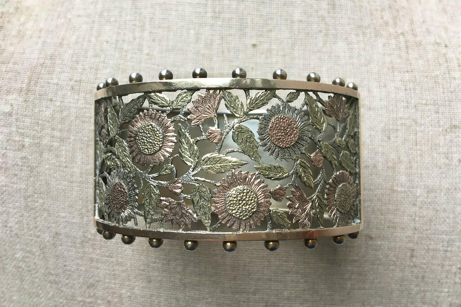 C.1883. A Victorian Aesthetic movement tri-color sterling silver bangle. The front panel of this wide bangle shows skillfully pierced flowers and leaves, and they are adorned with rose and green gold. With sterling silver, it makes a beautiful