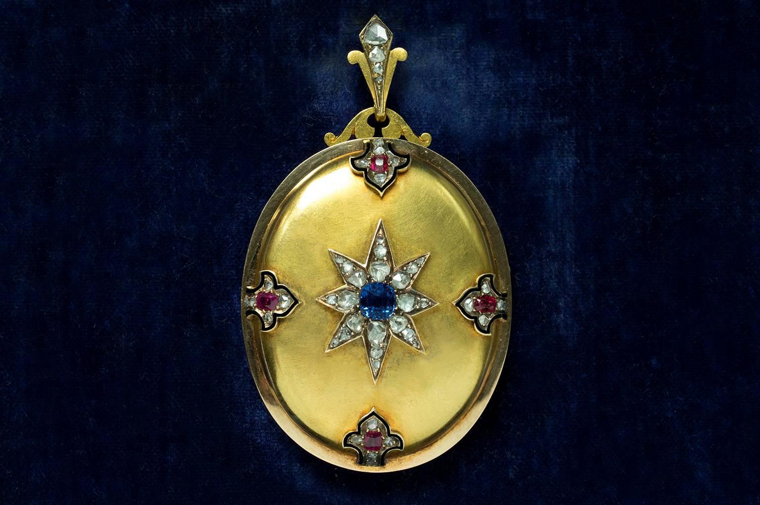 C.1880. A gorgeous late Victorian gold locket with a starburst center piece with a sapphire of beautiful cornflower color and rose cut diamonds. The locket is adorned with ruby, diamonds and black enamel at four additional points.  The rubies are in