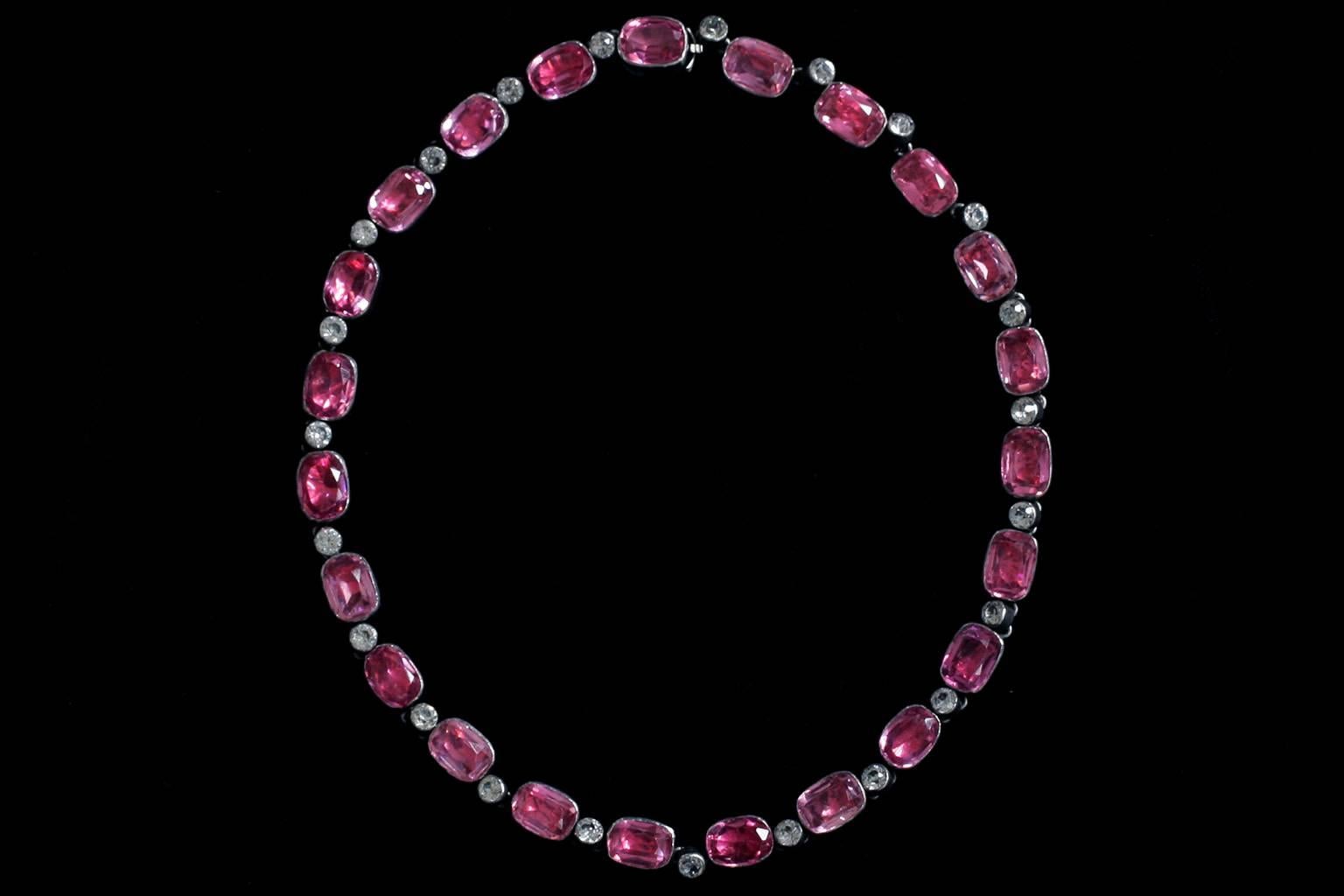 A very pretty late Edwardian/early Art Deco pink-and-white paste rivière necklace. Set in silver, each pink stone is vivid and bright, and the white diamond paste stones are colorless and clear. The necklace has a closed back setting, and contains