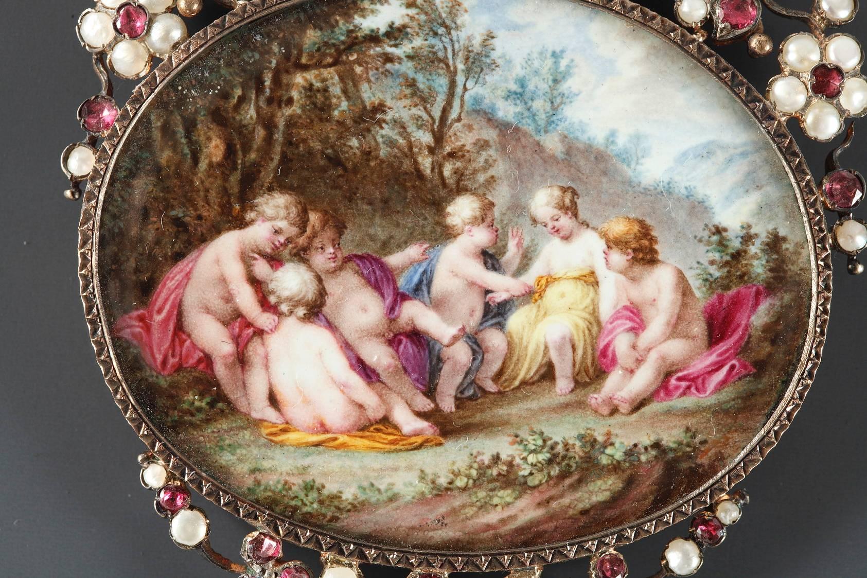 Napoleon III oval pendant with enamel scene depicting a group of putti in a landscape. A compartment with a glass door opens in the back for inserting a picture or a lock of hair. The openwork silver-gilt frame is embellished with flowers and