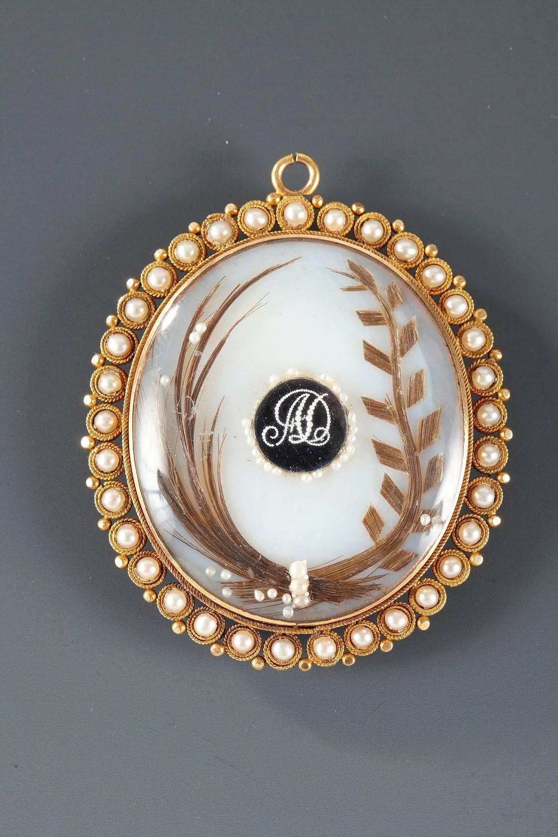 Mother of pearl medallion depicting a refined young gentleman on a light pink background. The pendant is mounted in gold that is set with pearls. The back is decorated with the monogram “AD” and locks of hair that are attached with delicate pearls.