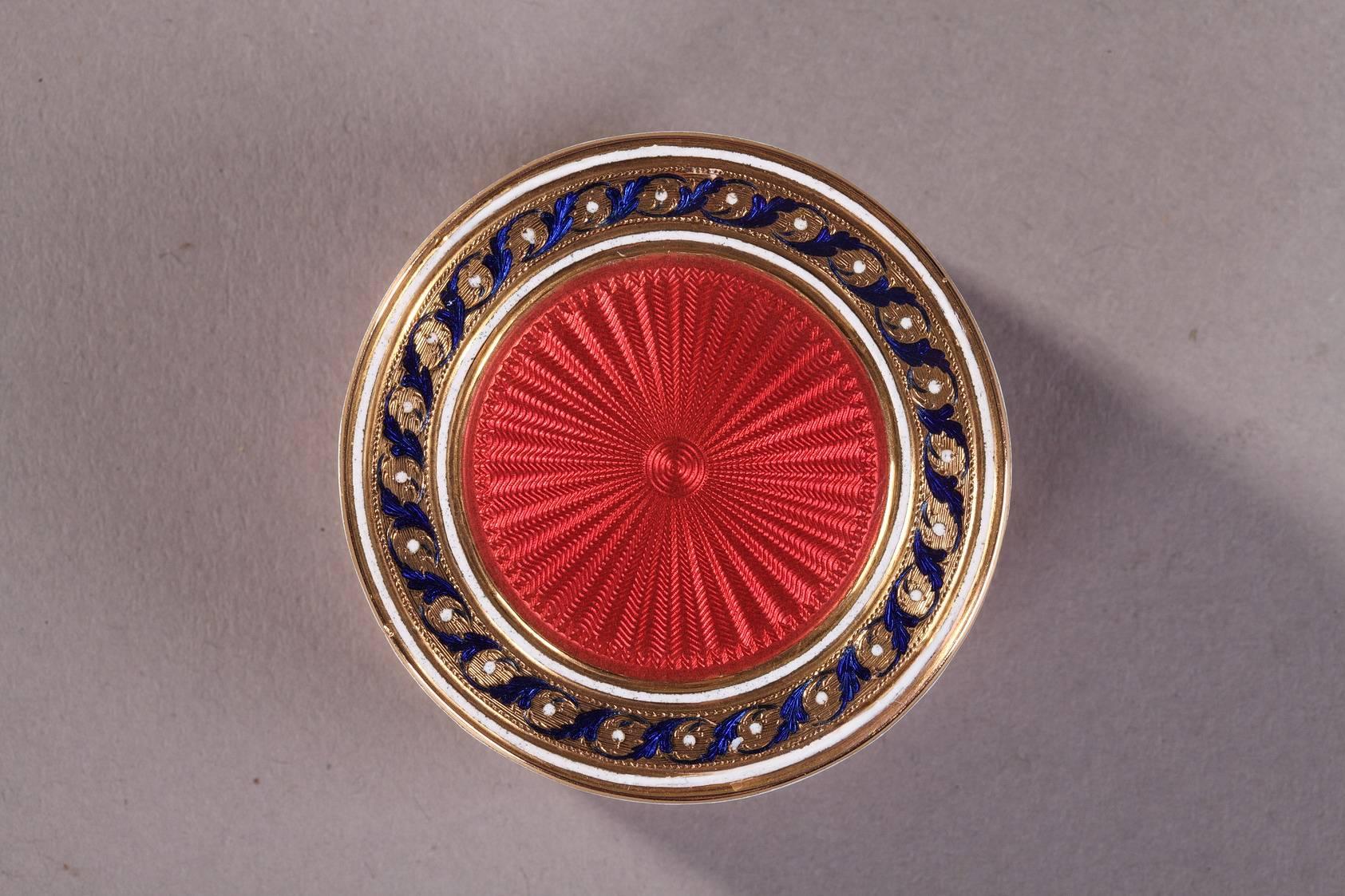 Circular box in pink enameled gold. The removable lid is embellished with an intricate starburst pattern, and the body and bottom of the box are decorated with a wave pattern. The translucent enamel leaves the intricate patterns in the gold