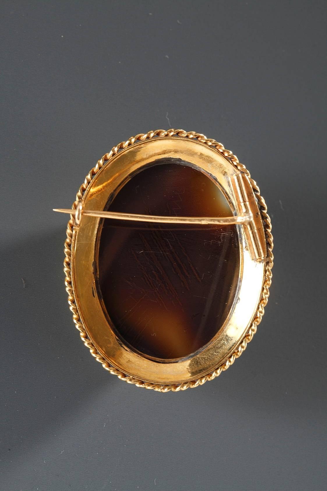 19th century oval agate brooch. It depicts the profile of a woman wearing a necklace and diamond earrings, set within a golden frame and accented with a ring of pearls. The sculpting of this brooch is very finely done. French mark “tête d’aigle”