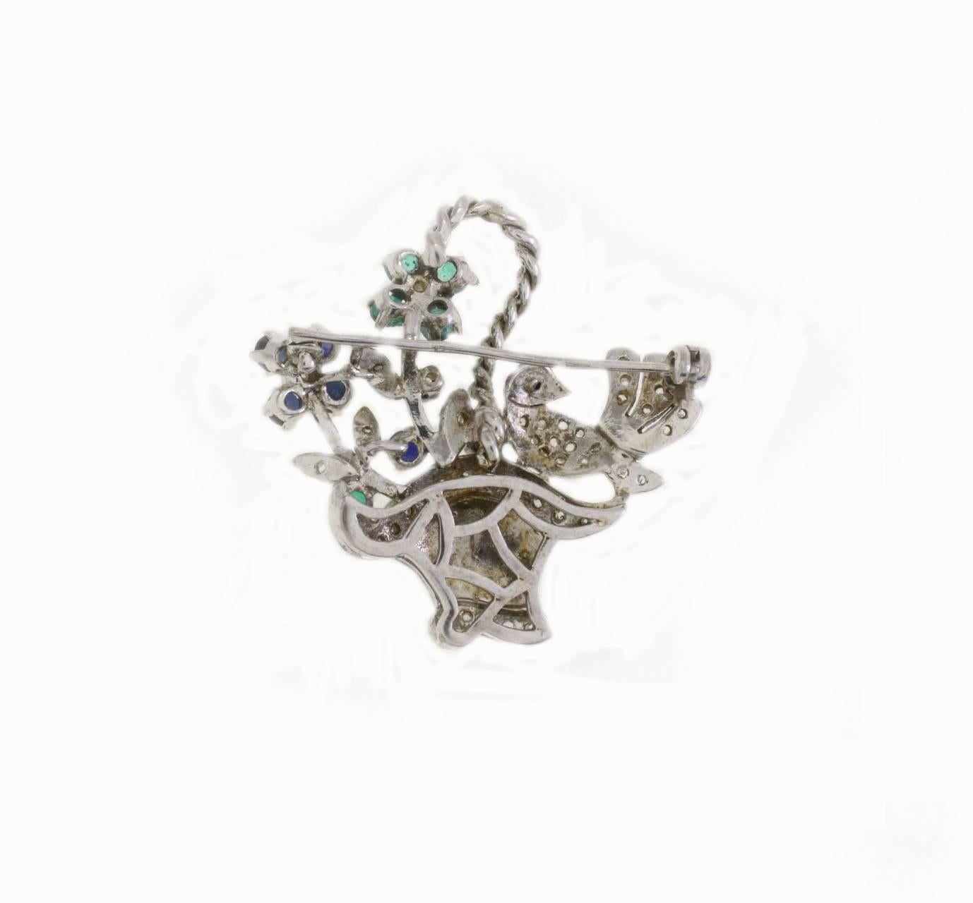 Graceful silouhette for this basket brooch, mounted on a base of 14K white gold (8.00gr) on it: a little bird and details in diamonds (0.34Kt)and flower of green sapphires and blue sapphires (1.78 Kt)  basket's color remain shiny during the time