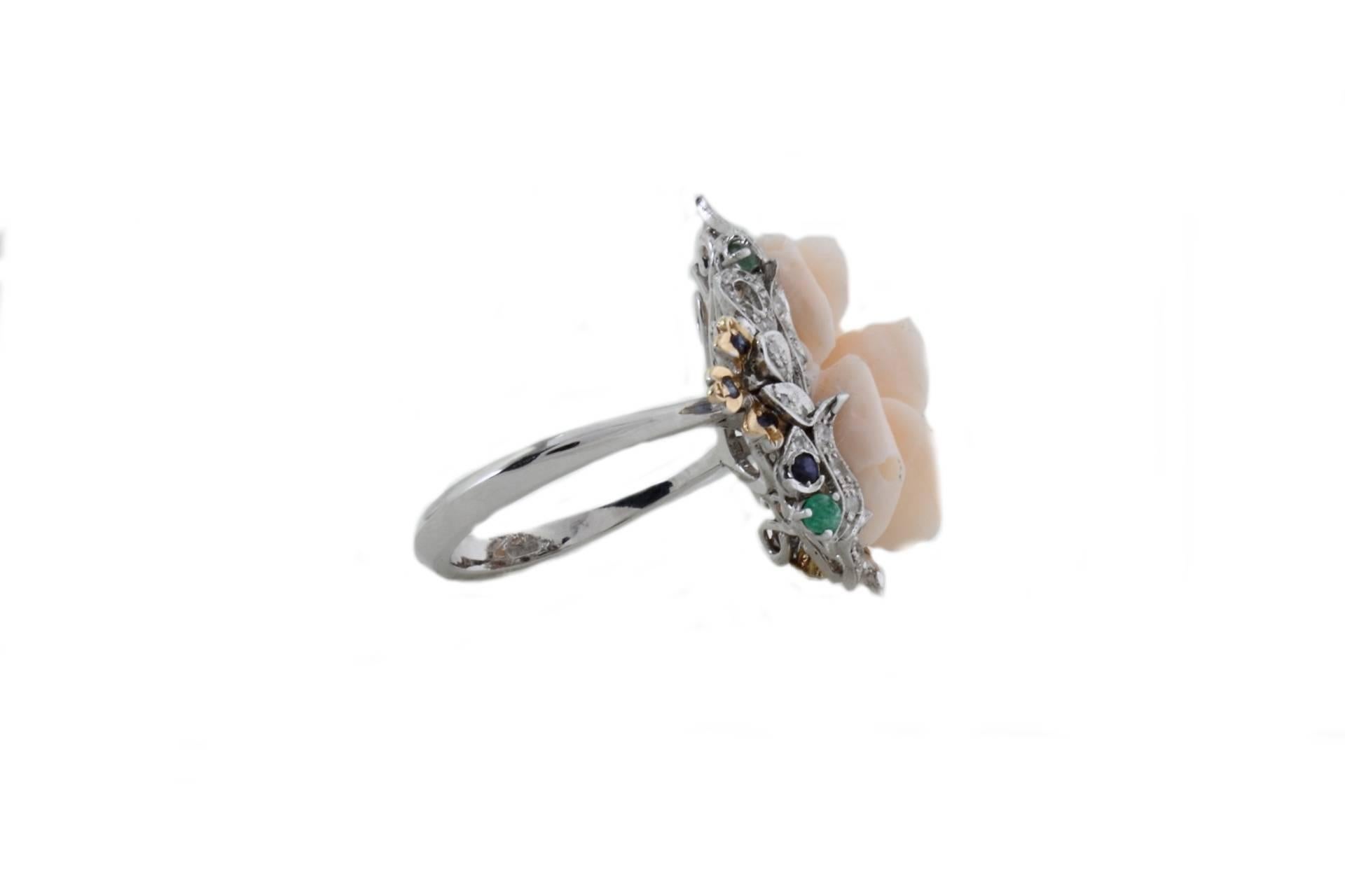 Classic and elegant ring with a crown of precious stones ( emerald, and multi blue sapphires for a tot carats of 0.19) with shiny  diamonds(0.60Kt), and a central rose shaped pink coral(2.70gr)   All in 14 Kt white gold and little details in 14K