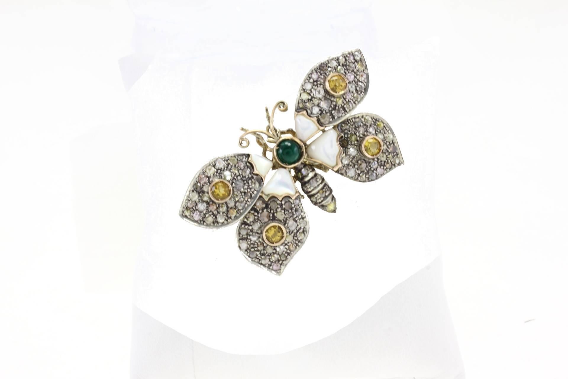 Butterfly shaped brooch/pendant in 9kt yellow gold and silver covered in rose cut fancy diamonds, 4 topazes a central emerald surrounded by mother of pearls.

gold 9.10gr
silver 8.40gr
diamonds 11.95kt
gems 2.53kt
mother of pearl 0.8gr
tot weight