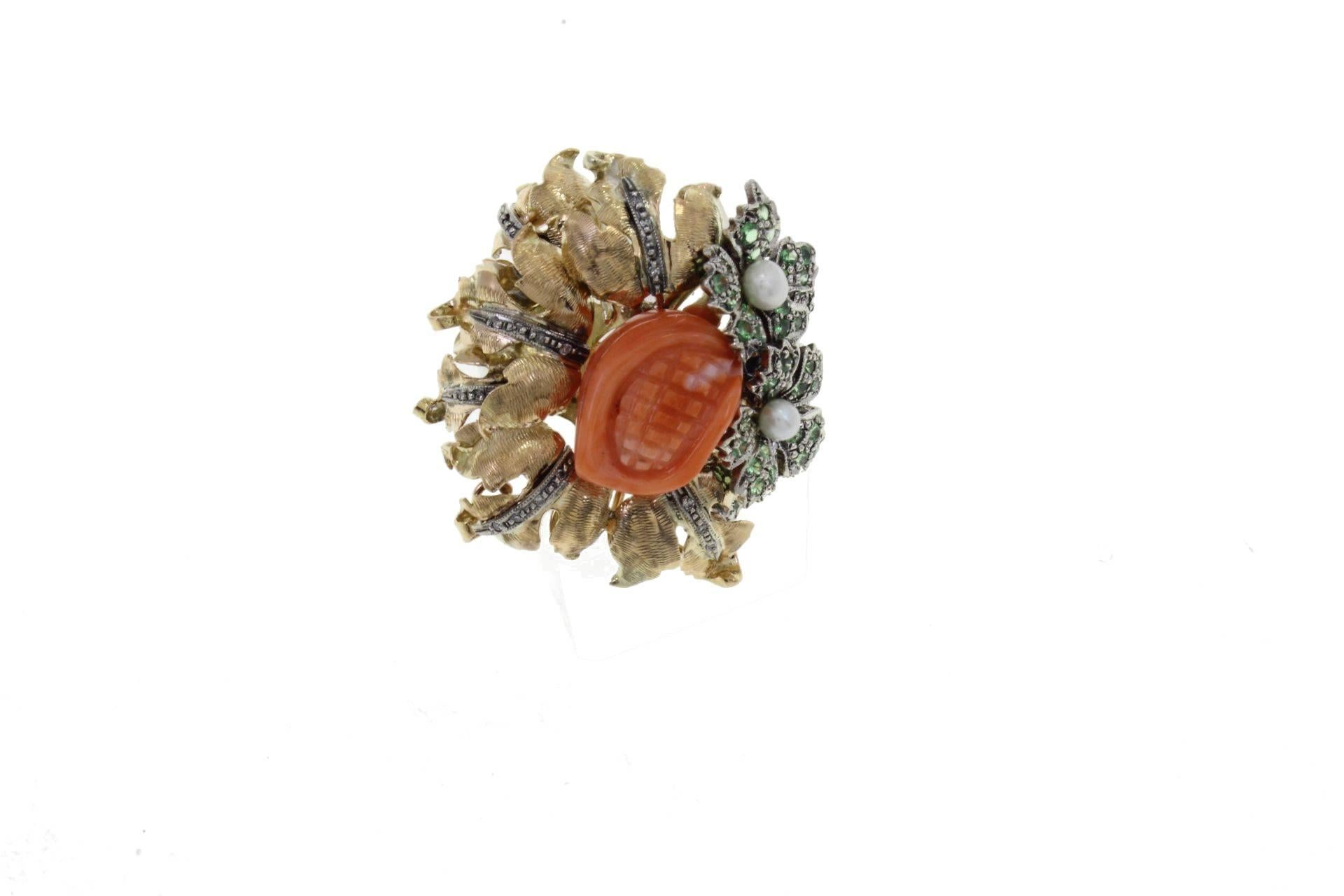 Cocktail ring in 9kt yellow gold and silver composed of a central carved coral surrounded by gold petals embellished with diamonds and flowers covered in tsavorite and pearl.
diamonds 0.10kt
tot weight 12.8gr
r.f.  uaci

For any enquires, please