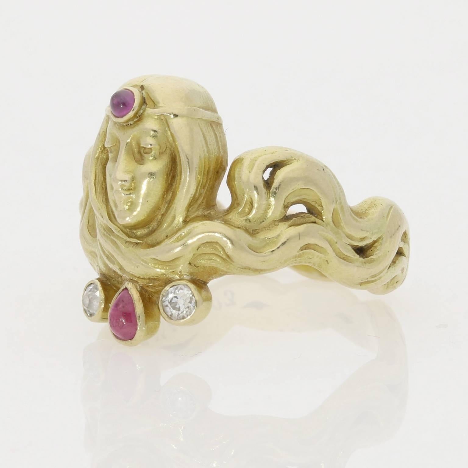 The heavy yellow gold ring modelled as a female head with luxurious flowing hair, highlighted with pink gold, entwined around the finger to form the band of the ring.  She wears a circlet around her forehead set to the centre with a cabochon ruby