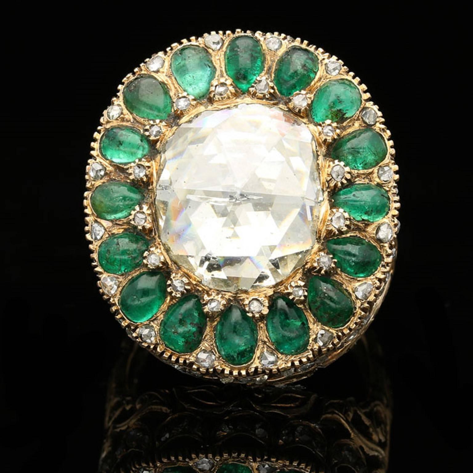 The ring centred on a large cushion shaped rose-cut diamond surrounded by sixteen pear shaped emerald cabochons in a cluster design embellished with two tiny rose-cut diamonds between each, all in a domed closed back setting, to a highly ornate