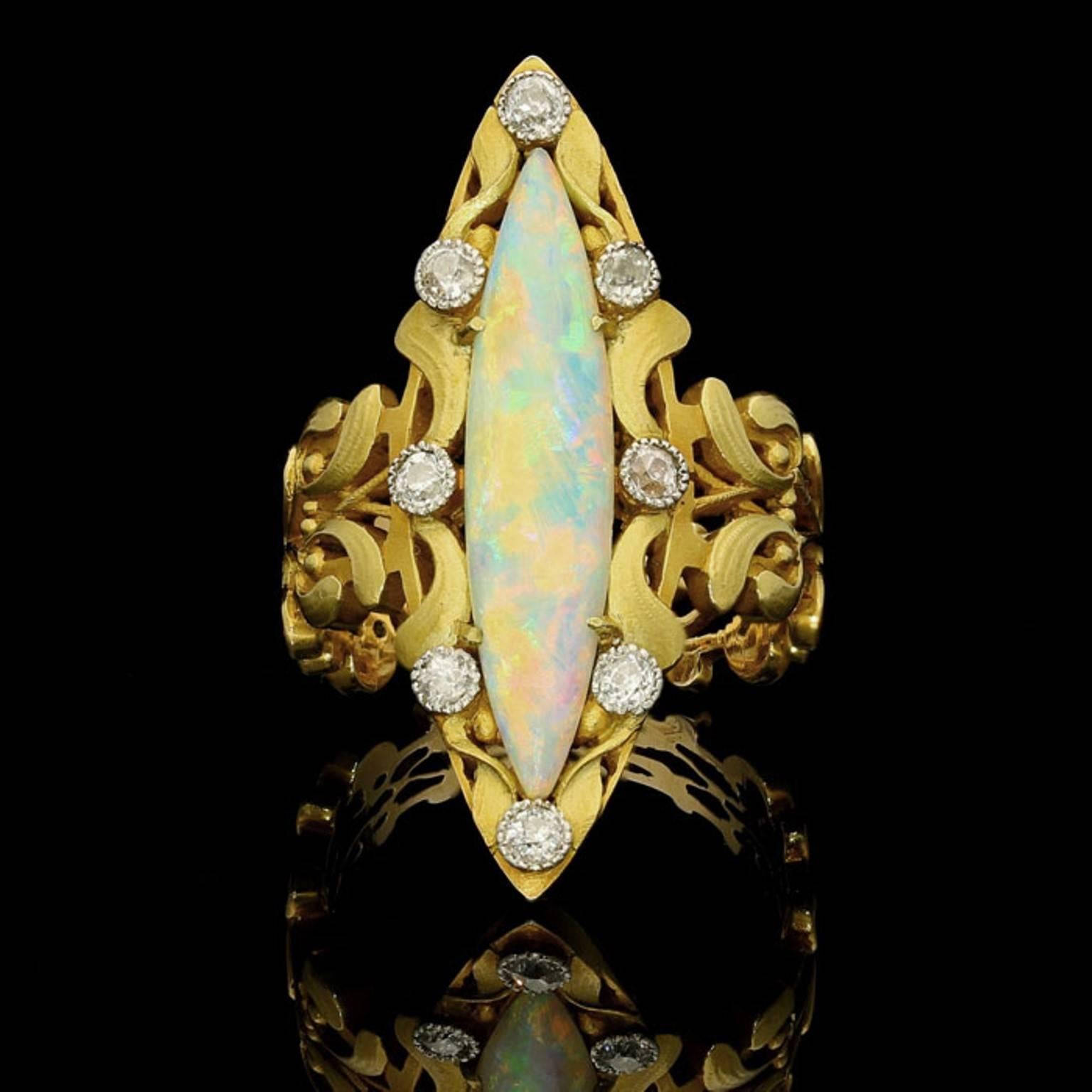 A beautiful Art Nouveau 18ct gold ring claw set with a narrow elongated marquise-shaped opal within an ornate gold openwork frame of mistletoe motifs highlighted with eight old-brilliant cut diamonds to a wide band of mistletoe garland
