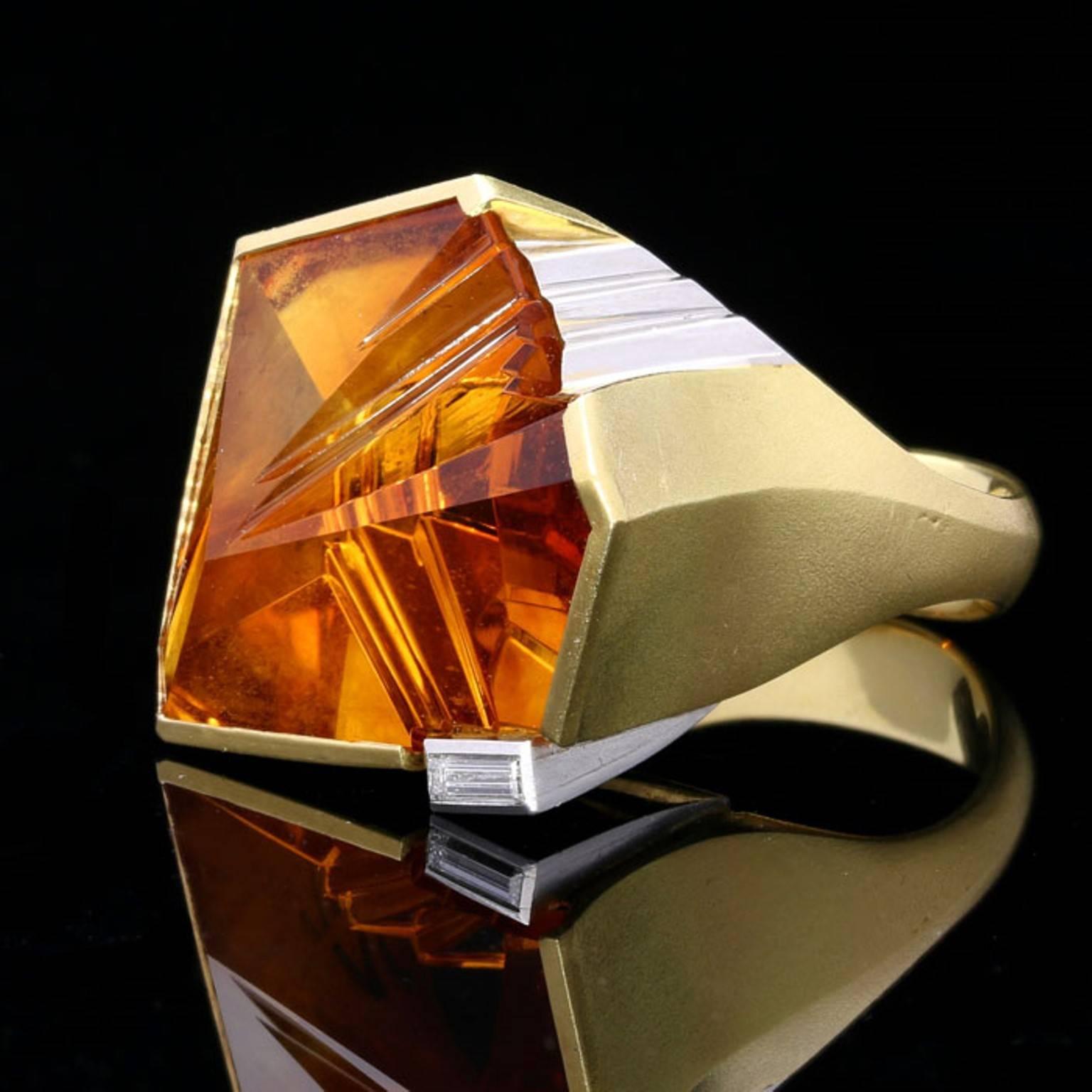 The large asymmetric geometric fantasy-cut citrine in a rub over yellow gold setting highlighted with a band of white gold and a small baguette cut diamond, the smooth enclosed gallery and tapered shank with a satin finish to the gold.

Asymmetric