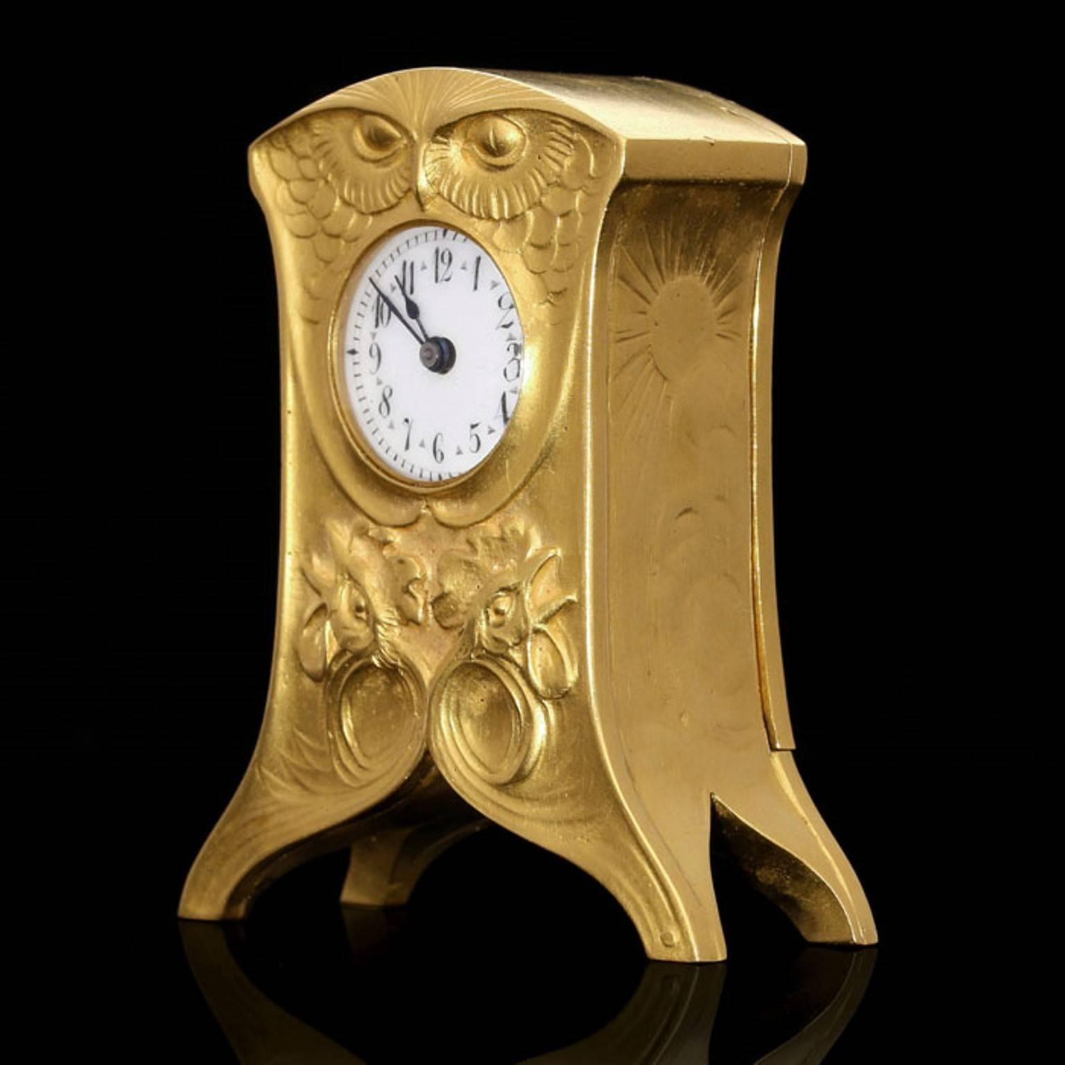 The clock in satin-finish 18ct yellow gold with detailed repoussé and chasing work in the Art Nouveau style depicting contrasting motifs all symbolic of day or night. The front with an owls head forming the top beneath which the dial is set, the