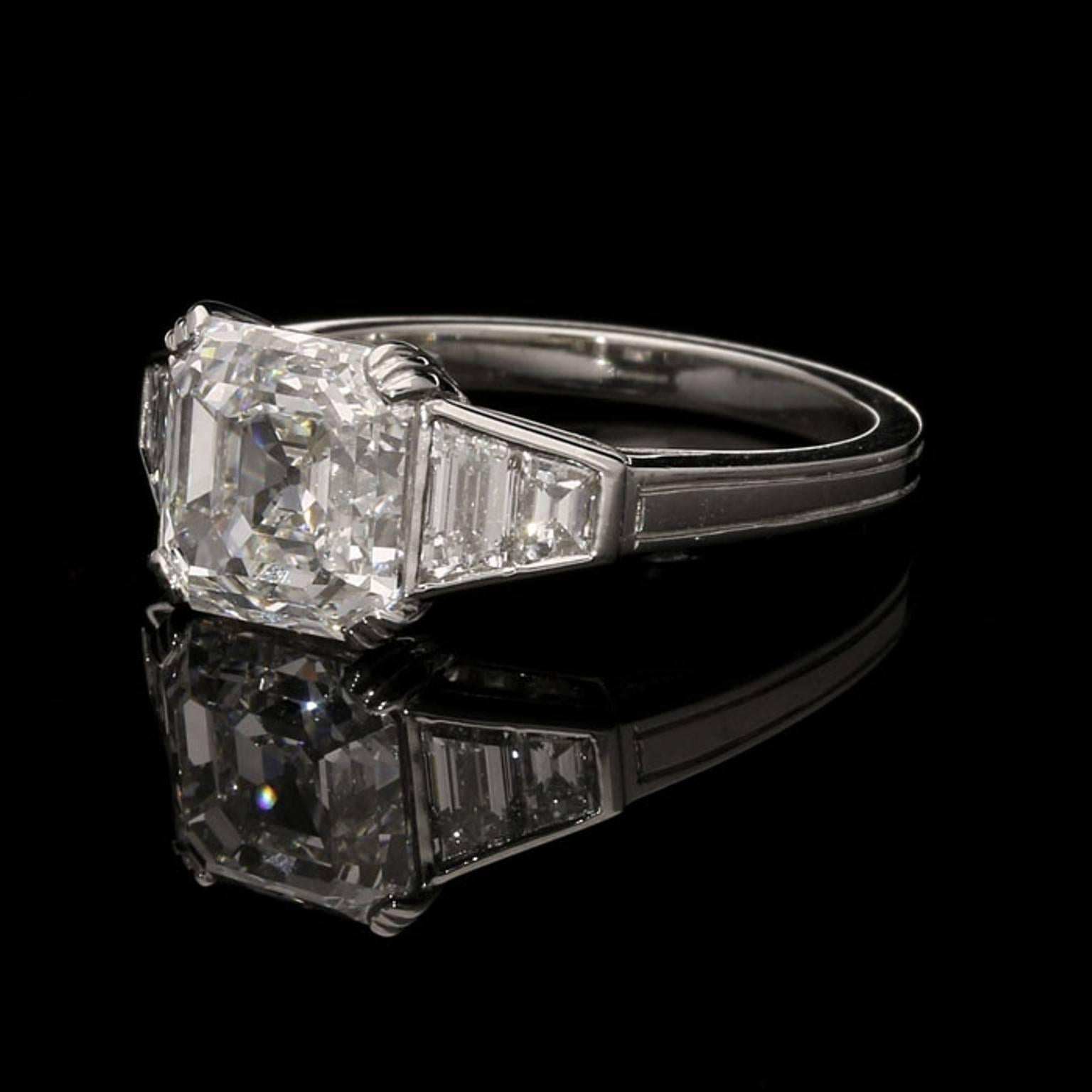 The ring centred on a beautiful square step cut diamond weighing 3.31cts and of G colour and VS2 clarity set to the corners with fluted claws in a fine handmade platinum mount, the shoulders rub over set with graduated trapezoid diamonds tapering to