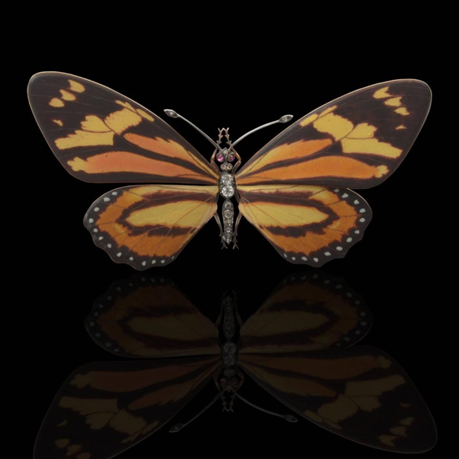 A rare enamel brooch in the form of a butterfly in flight its wings in polychrome enamel with a satin finish, the thorax, abdomen and antennae set with European brilliants and rose-cut diamonds and the eyes with cabochon rubies mounted in silver and