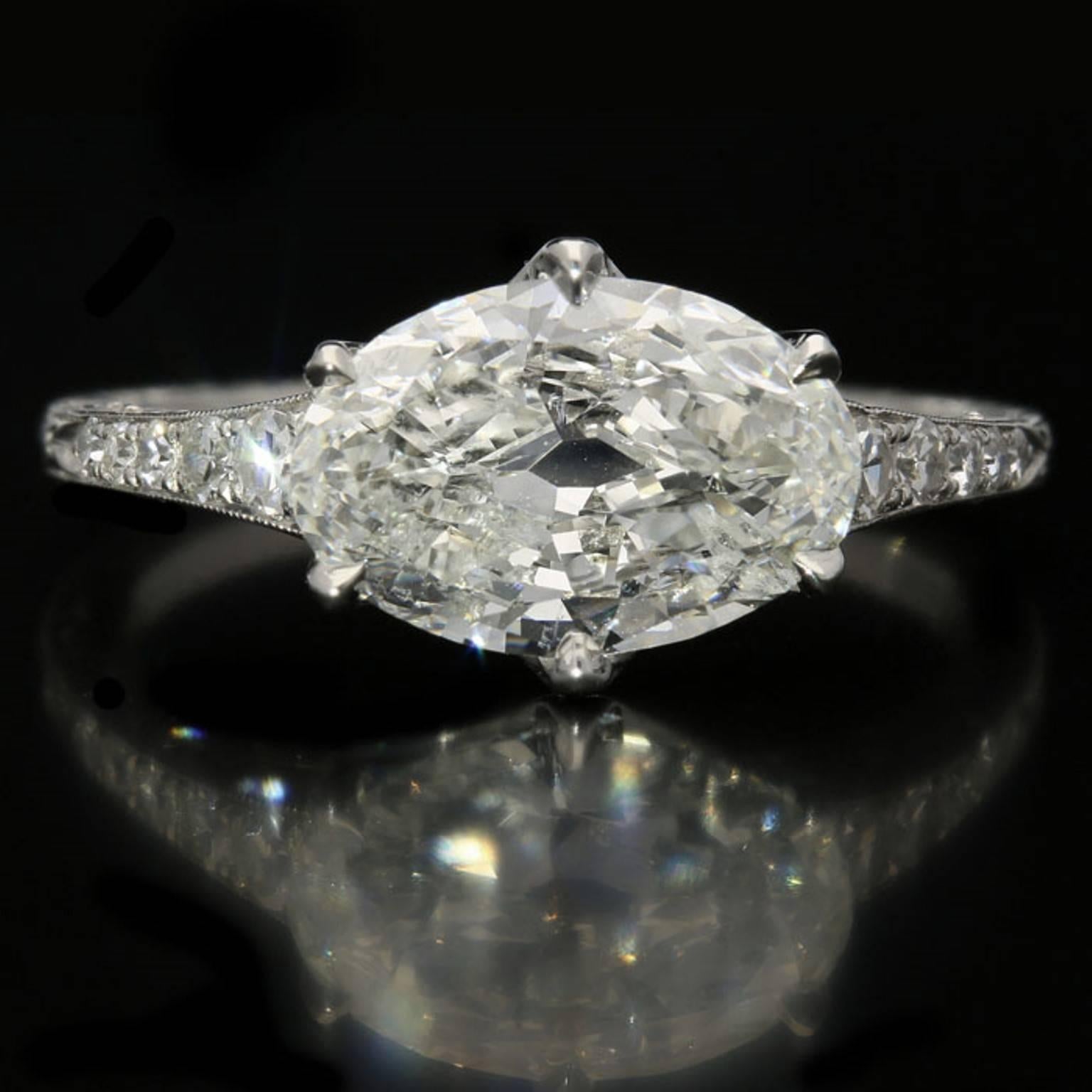 The ring designed around a lovely moval shaped old- cut diamond weighing 2.04ct and of G colour and I1 clarity set horizontally across the finger within a six claw, finely scalloped platinum mount with ornate scrolled hand engraving and tapering