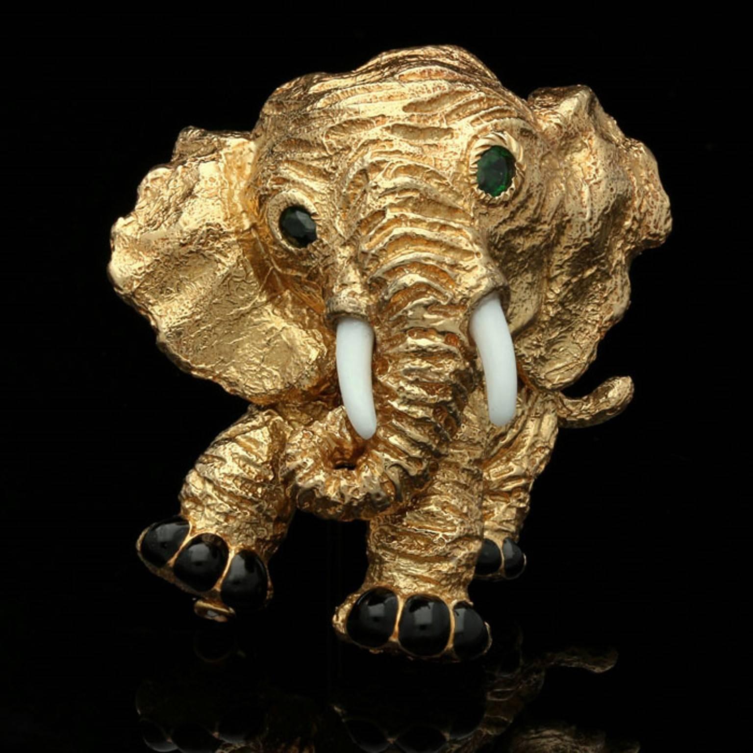 The delightful brooch finely modelled in textured 18ct yellow gold as an elephant with his head tilted to one side and tail held jauntily aloft, the eyes set with emeralds, the tusks carved from white agate and feet in black enamel.

18ct yellow