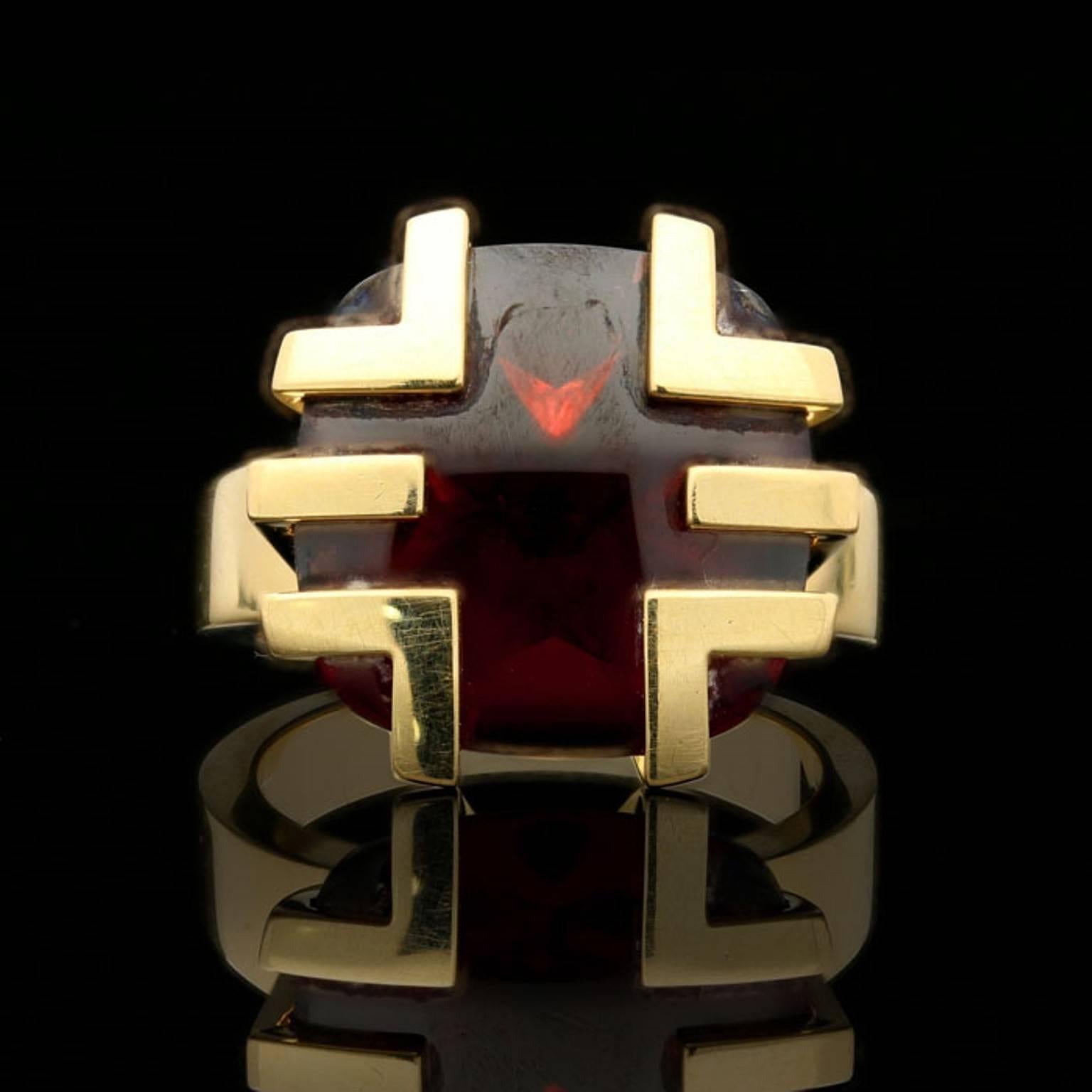 A stylish 18 carat yellow gold and garnet ring by Cartier, c. 2003, from the 'Le Baiser du Dragon' (Kiss of the Dragon) collection, designed as a cushion shaped buff top garnet set to the corners and sides with angular geometric gold motifs to a
