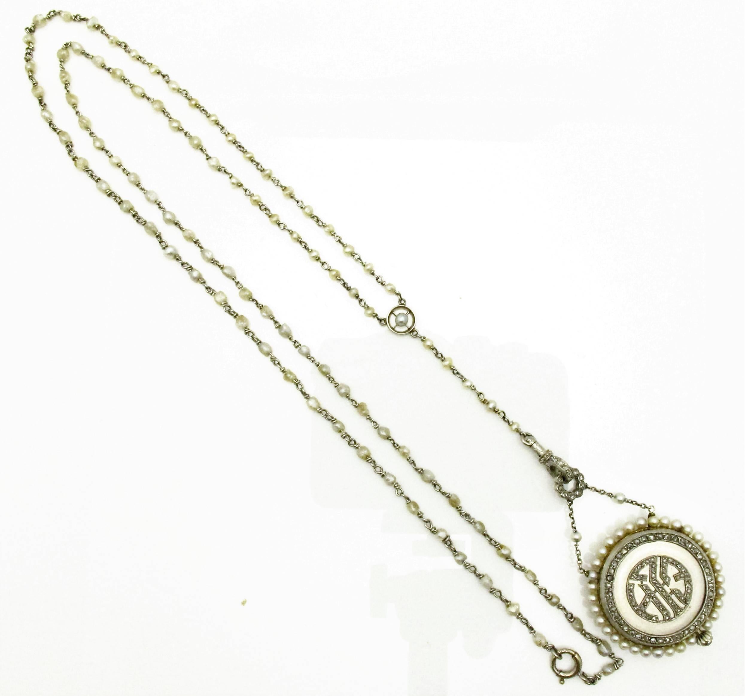 Stunning Edwardian platinum, diamond and seed pearl watch pendant necklace. The platinum link chain set with interspersed seed pearls that terminate to a watch pendant drop. The watch pendant, with working movement, features a diamond set monogram