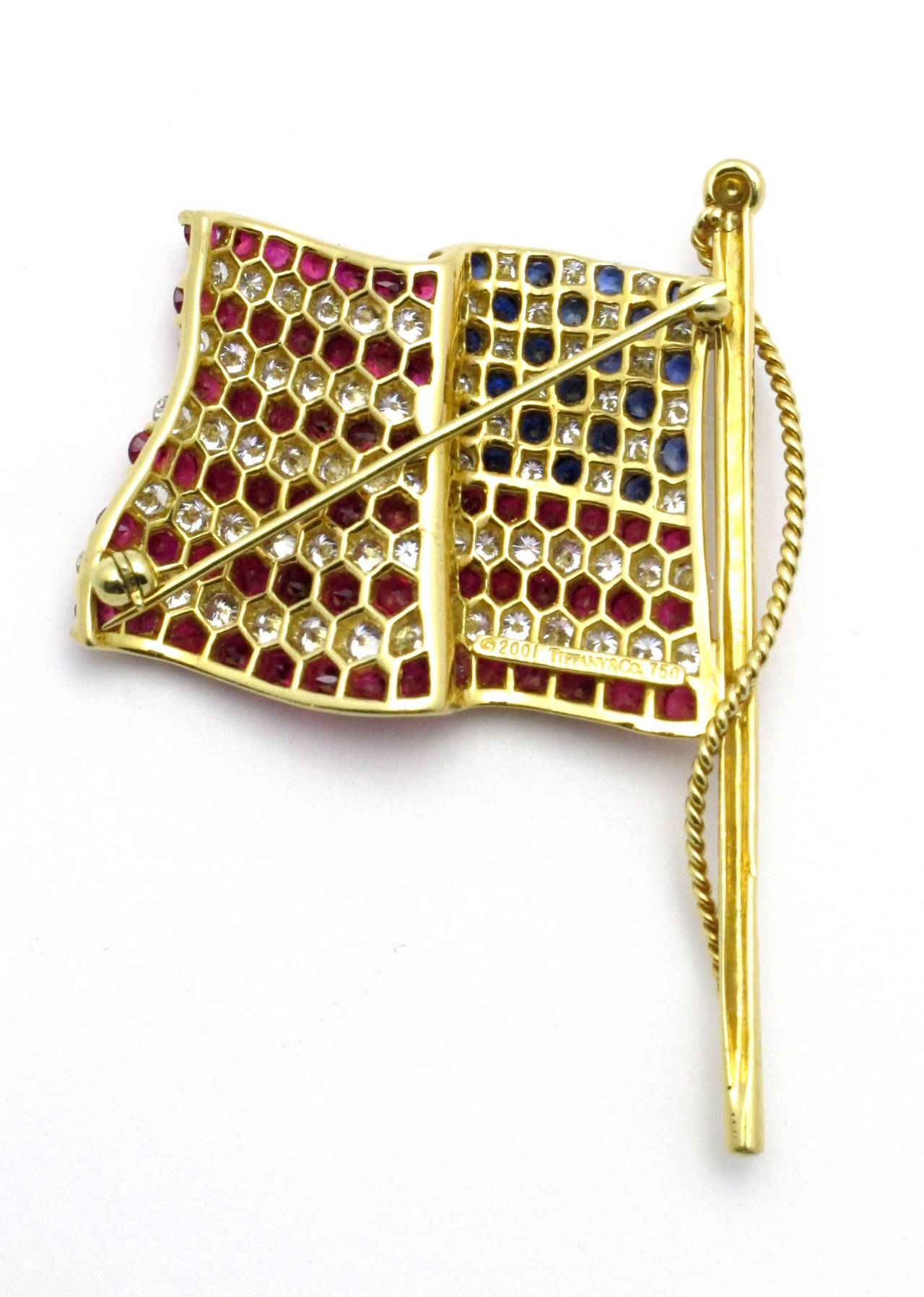 Designed as a waving American flag, this Tiffany & Co. 18kt yellow gold flag brooch is beautifully adorned with modern round brilliant-cut diamonds, rubies, and blue sapphires.

The flag is set with approximately:
73 diamonds of total weight