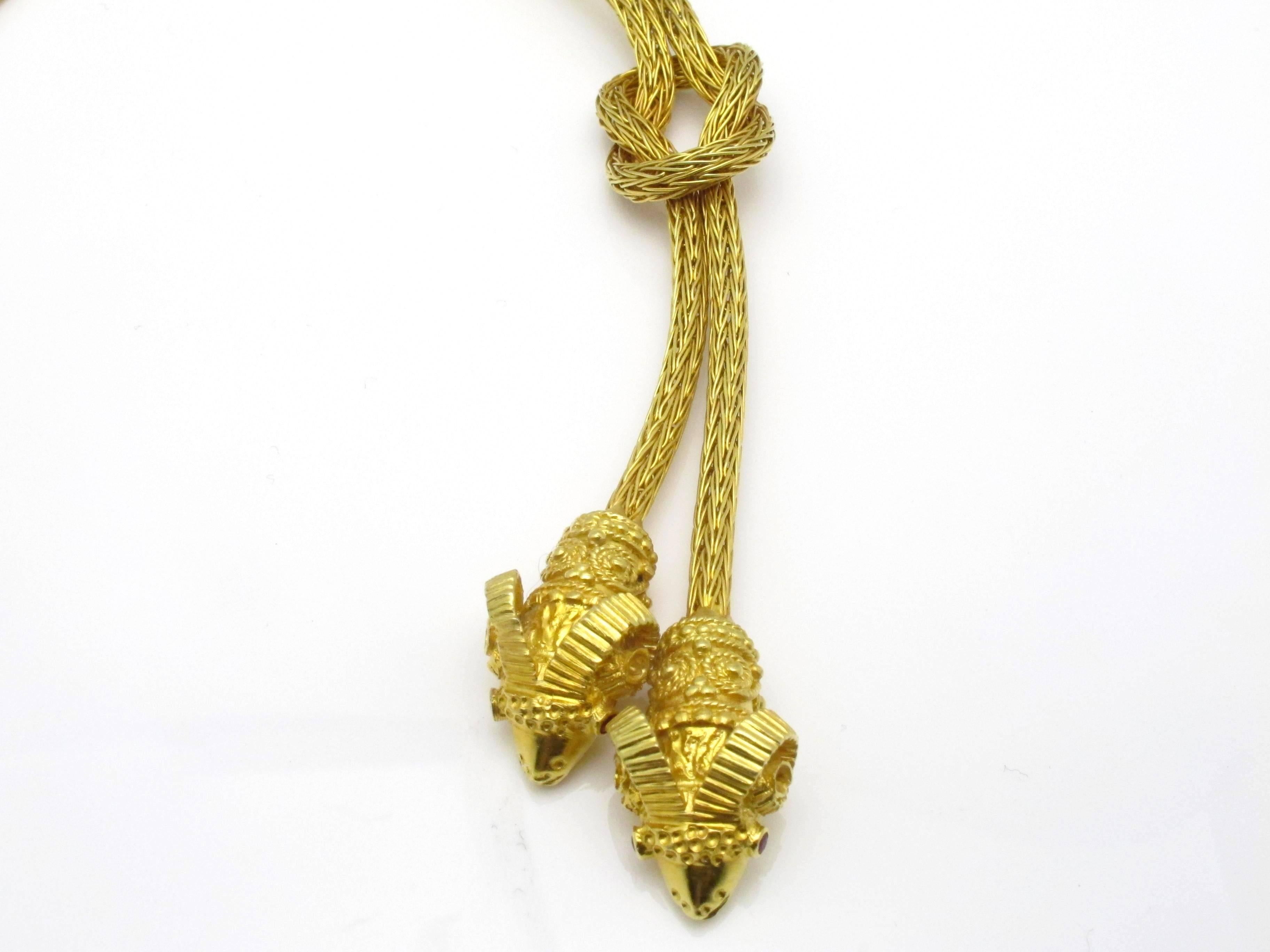 Beautiful Ilias Lalaounis woven gold necklace featuring two rams head drops set with ruby eyes suspended from a herculean knot.  
Length from knot to head: 3.25