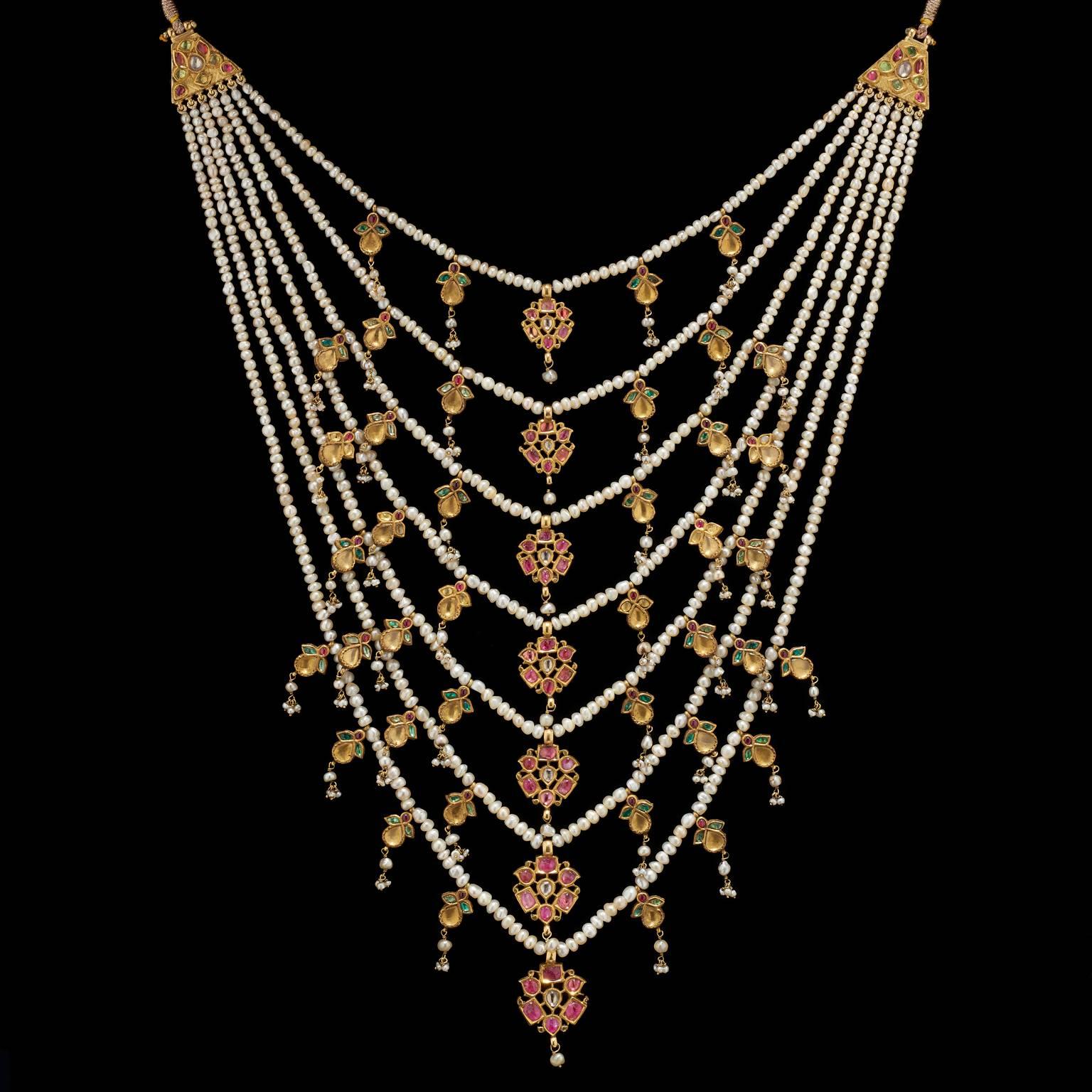 Necklace
Mughal, North India
18th Century

A seven row (satlara) necklace set on seven strings of natural pearls. The central pendants are gold set with rubies and emeralds forming stylized floral motifs. Each strand has smaller pendants on