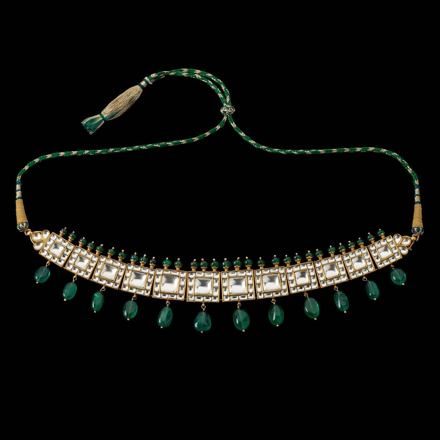 Necklace
Jaipur, Rajasthan, India
20th Century

Fabricated from gold, the necklace has square panels set with rock crystal in a square arrangement, each plaque suspending an emerald drop and surmounted with a fringe of emerald beads. The reverse