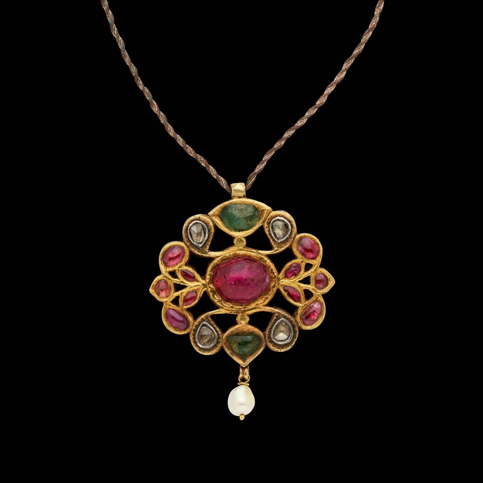 Pendant
Gujrat, Western India
Early 19th century

Fabricated from gold, set in kundan (traditional pure gold setting) technique with diamonds, emeralds and a central cabochon ruby, with pendant pearl. The reverse is plain gold.


