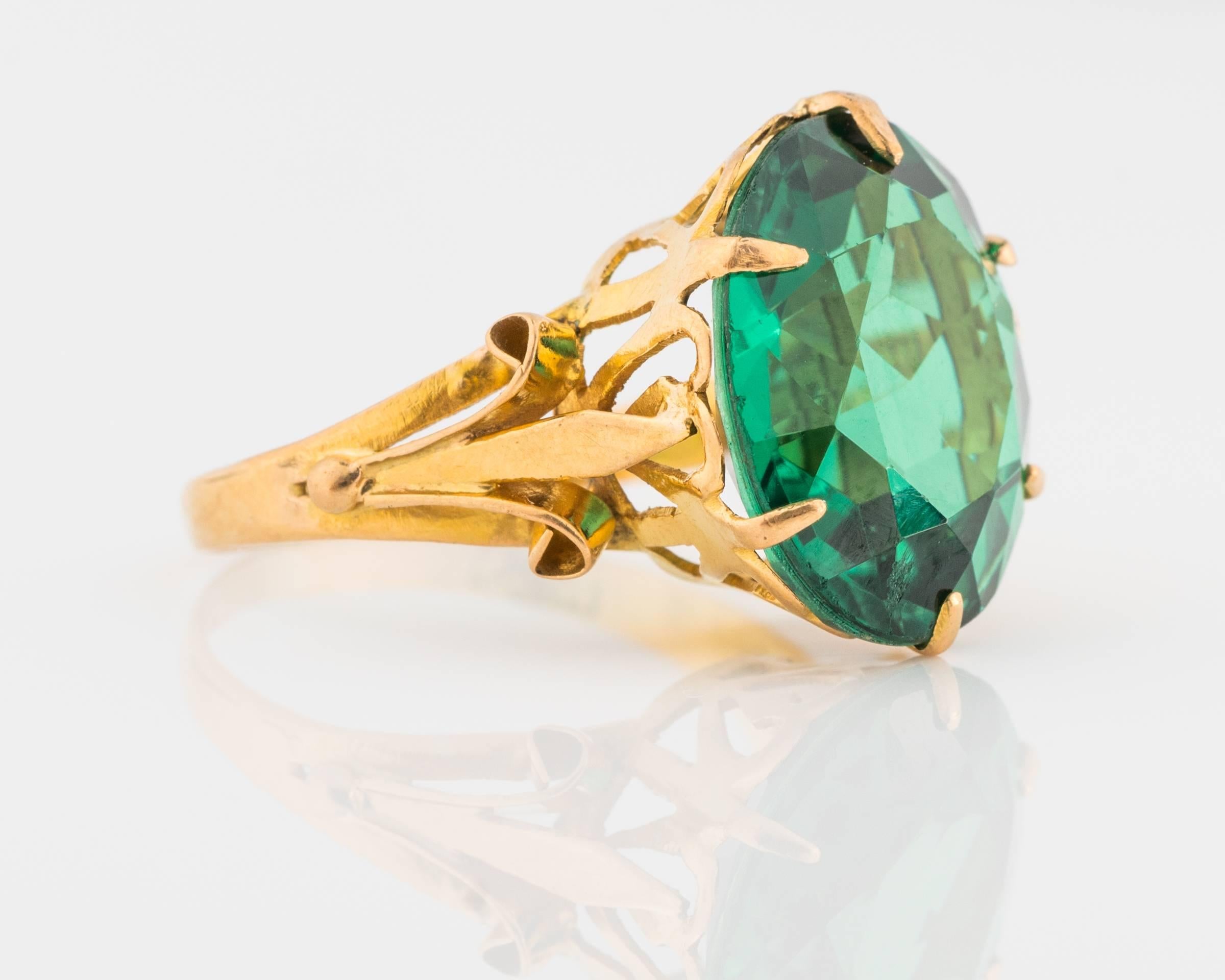 1890s Emerald and 21.6 karat yellow gold ring. Center features a large green simulated emerald stone. Stunning deep green hues are visible in this emerald, mystical appearance. Minor abrasions on the stone, considering the age of the ring. Emerald