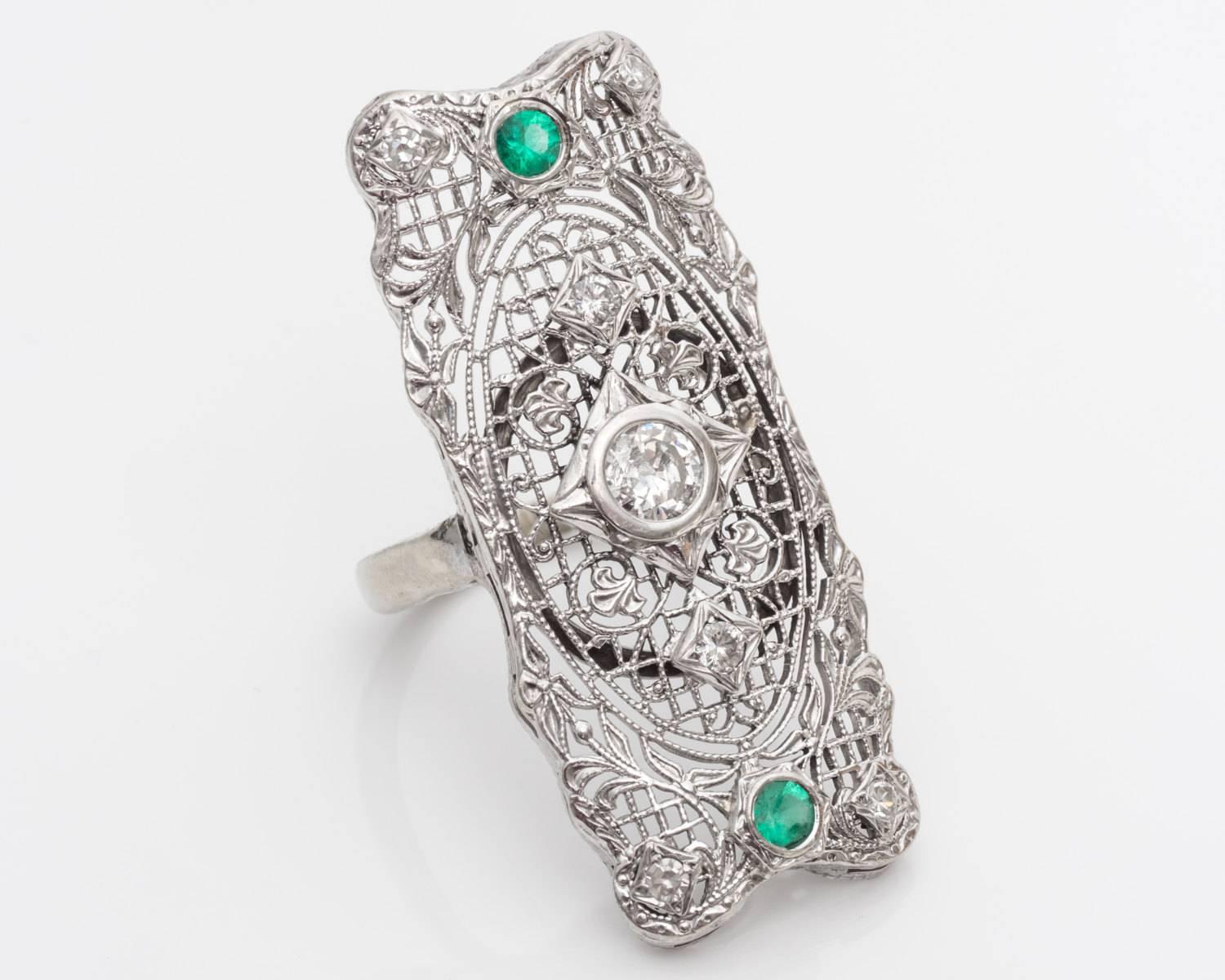 14 Karat White Gold Filigree Shield Ring
Full of Intense and Delicate Filigree Scroll Design 
Features Diamonds and Emeralds
Fits Ring Size 7, Resizable


Center Diamond Details: Transitional Cut round, Weighs 0.33 Carats, G Color, SI1 Clarity,