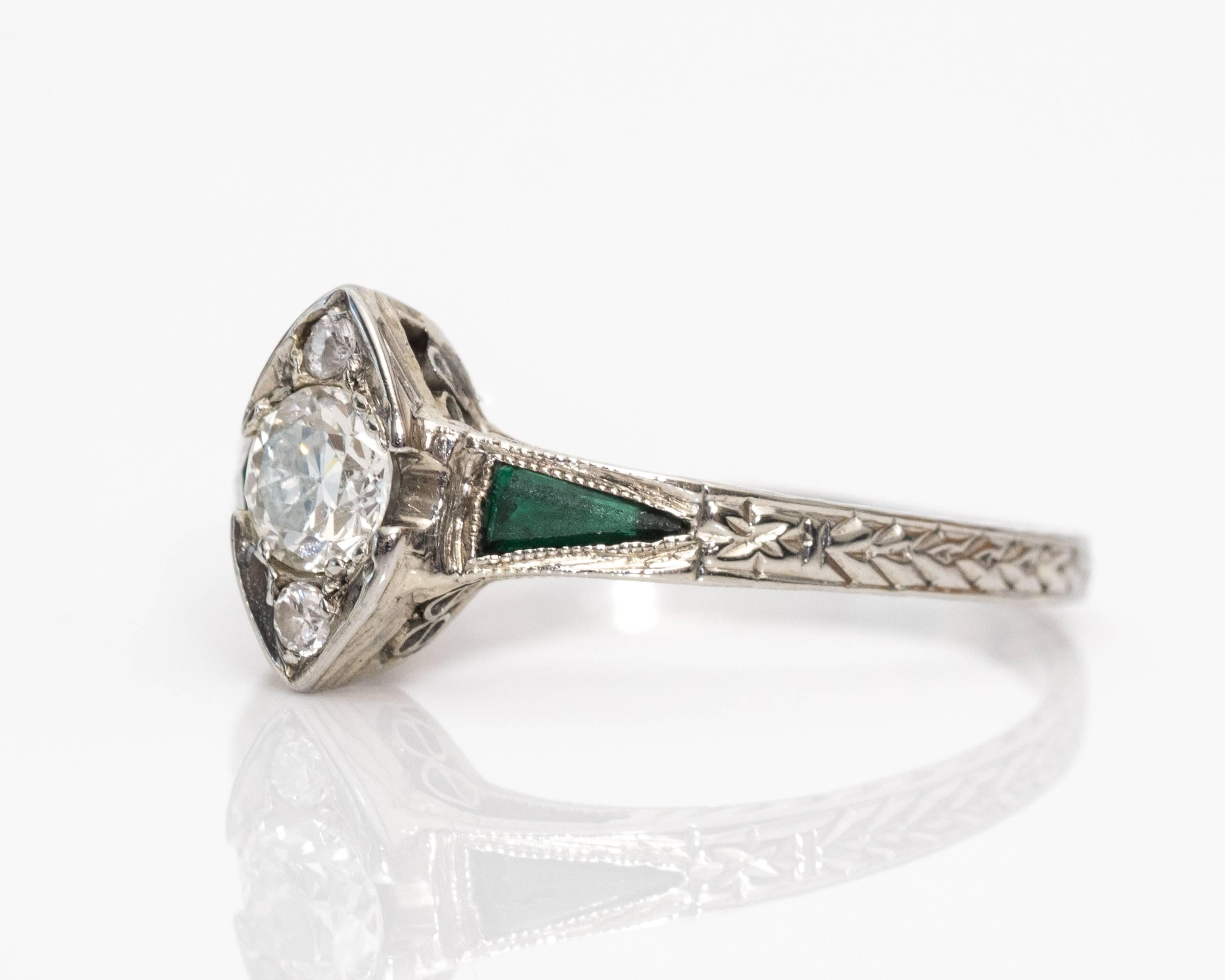 1915 Art Deco .20 Carat Old European Diamond Emerald 18 Karat White Gold Ring features an Old European Diamond (0.20 carat) center stone with Two Accent Diamonds on Top and Bottom. Marquise Shaped Bezel Places the Ring Together in a Single Setting,