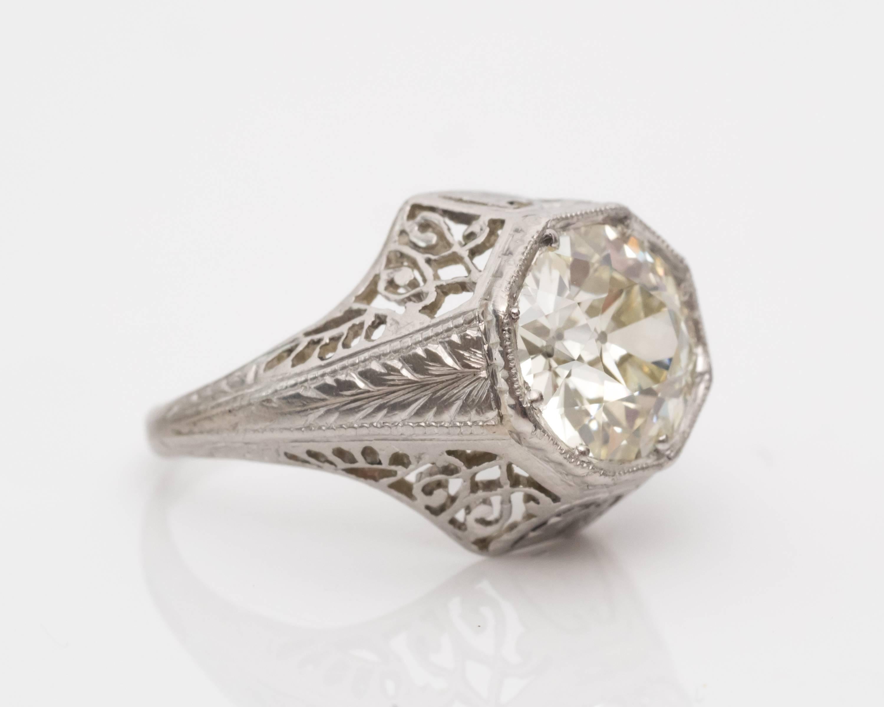 1920s Art Deco GIA 1.45 Carat Old European Diamond Platinum Engagement Ring. Set in a Stunning Milgrain Bezel Frame surrounded by Heavy Intricate Filigree and Cutouts, visible on all sides. The shoulders of the ring feature leaf designs etched into