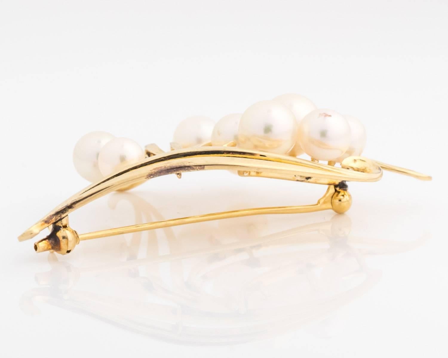 1960s Mikimoto Pearl Brooch features 14K Yellow Gold and 10 pearls in assorted sizes arranged in 3 clusters. The pearl clusters are framed by three 14 karat gold strand leaves. The gold strands form linear curves which taper to elegant swirls at