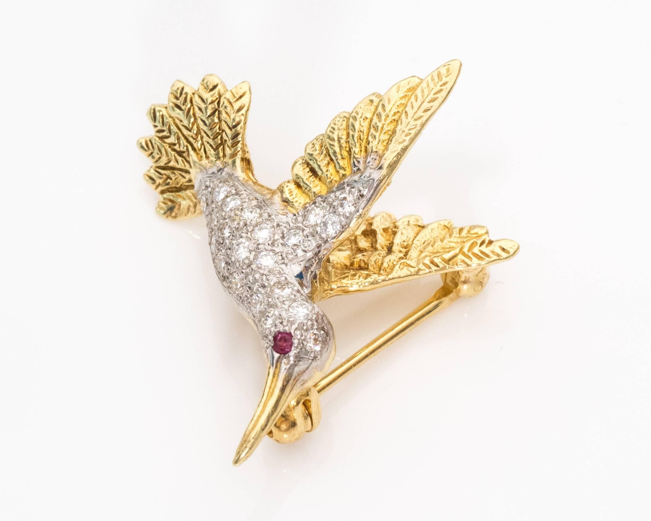 1980s Vintage Hummingbird Brooch features 18K Yellow Gold, .20 carats of diamonds and .01 carat Ruby. The bird is covered in diamonds and has a Ruby eye. The 18K gold wings and tail have a detailed feather texture. The gold beak is smooth with a
